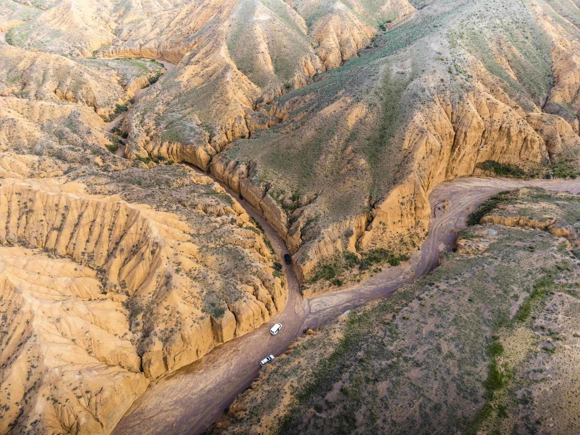Aerial view of 4x4s driving through winding canyons and clay hills in Kyrgyzstan.