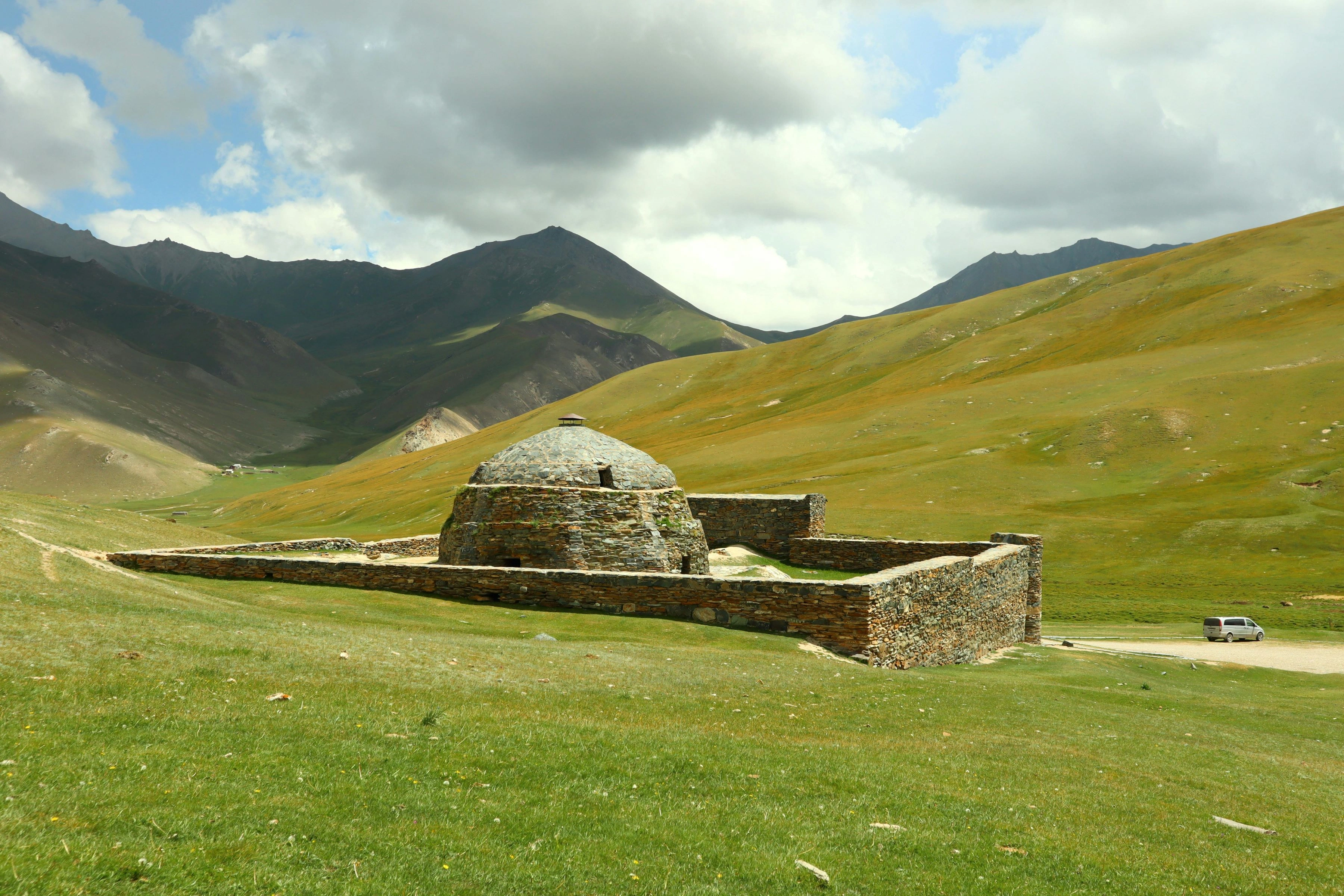 Ancient stone building in green Kyrgyz valley surrounded by rolling hills and mountains.