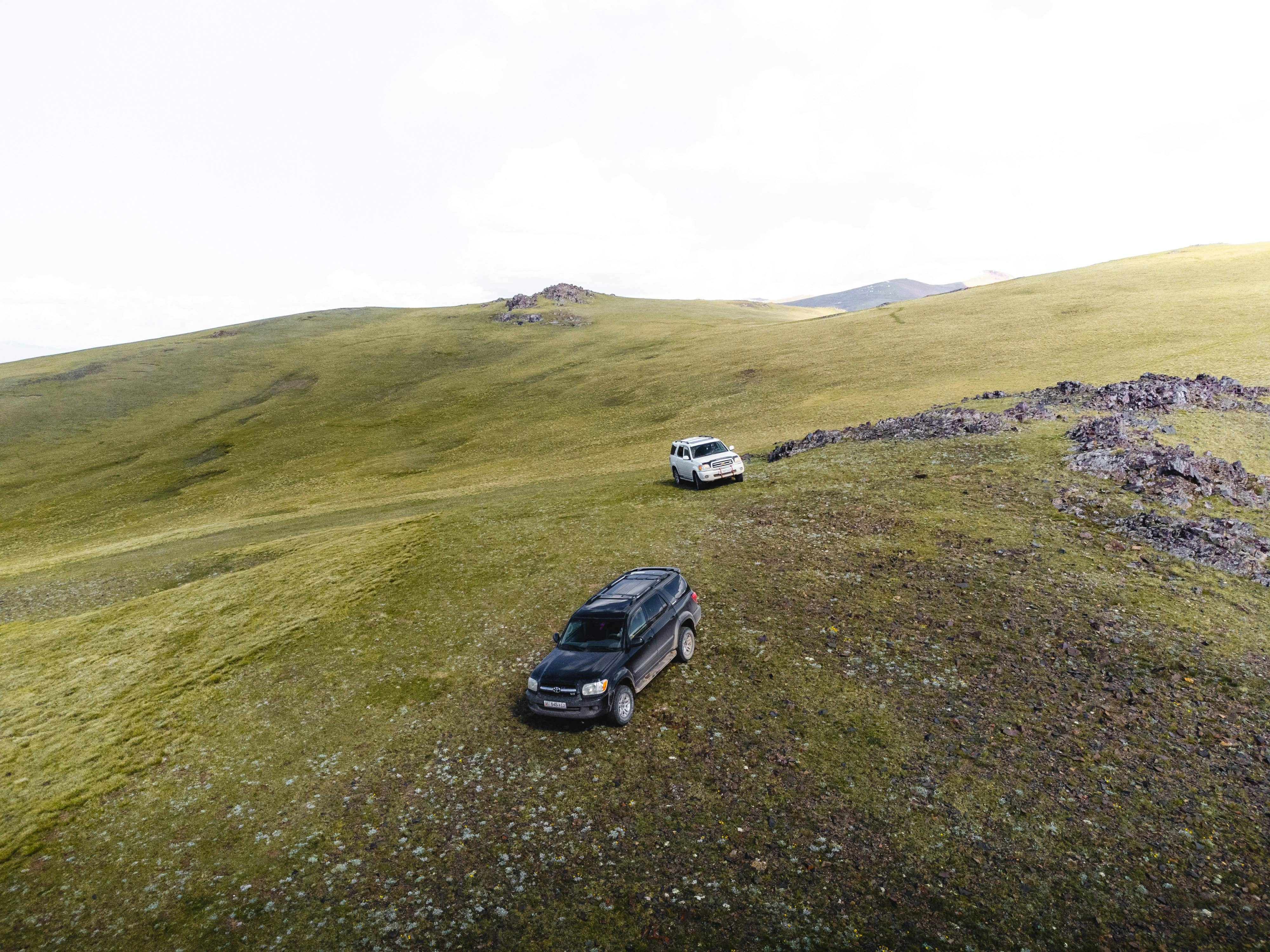 Two off-road vehicles parked on grassy Kyrgyz plateau surrounded by rolling hills.