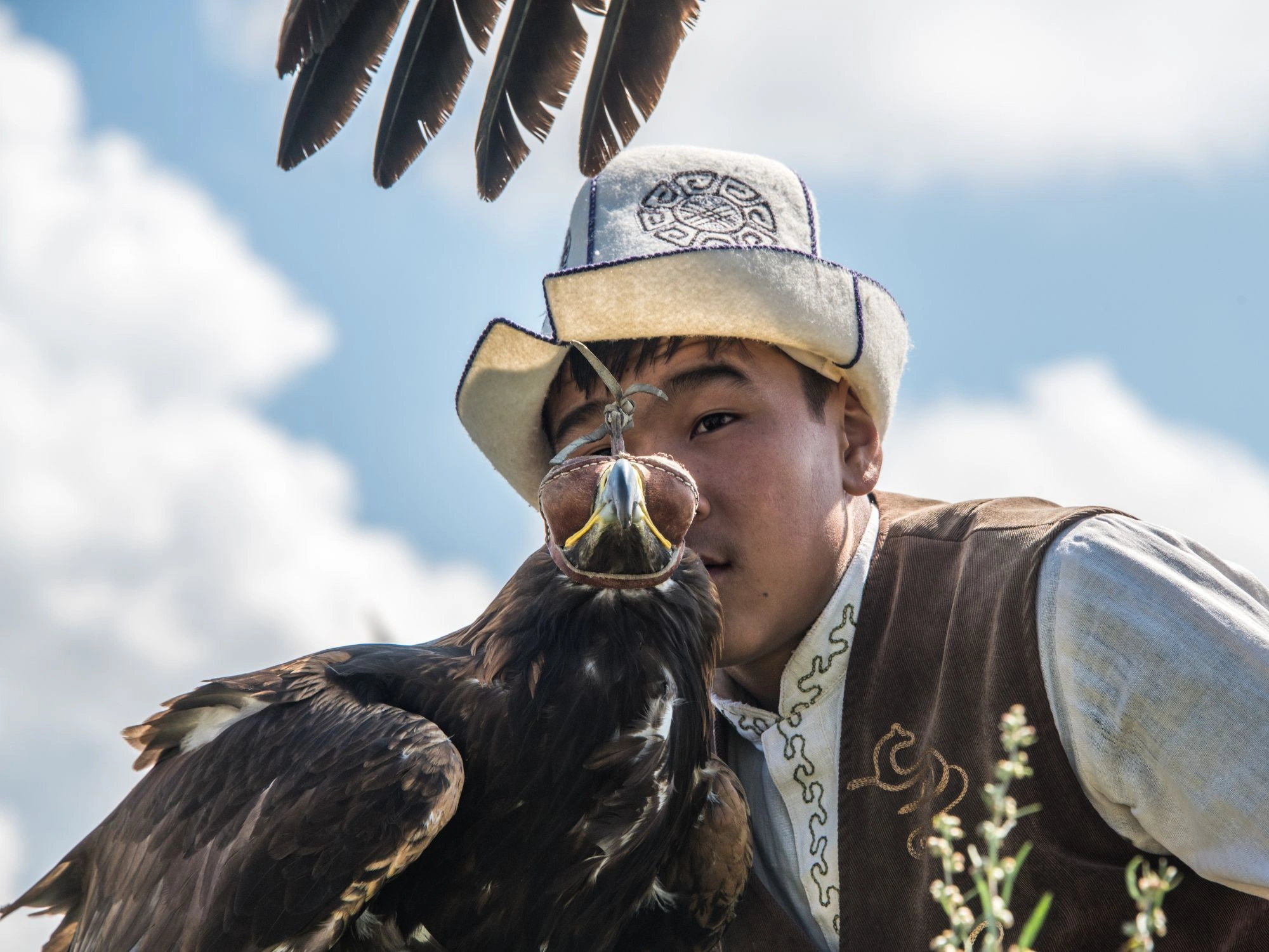 Kyrgyz eagle hunter in traditional attire with golden eagle perched on gloved arm.