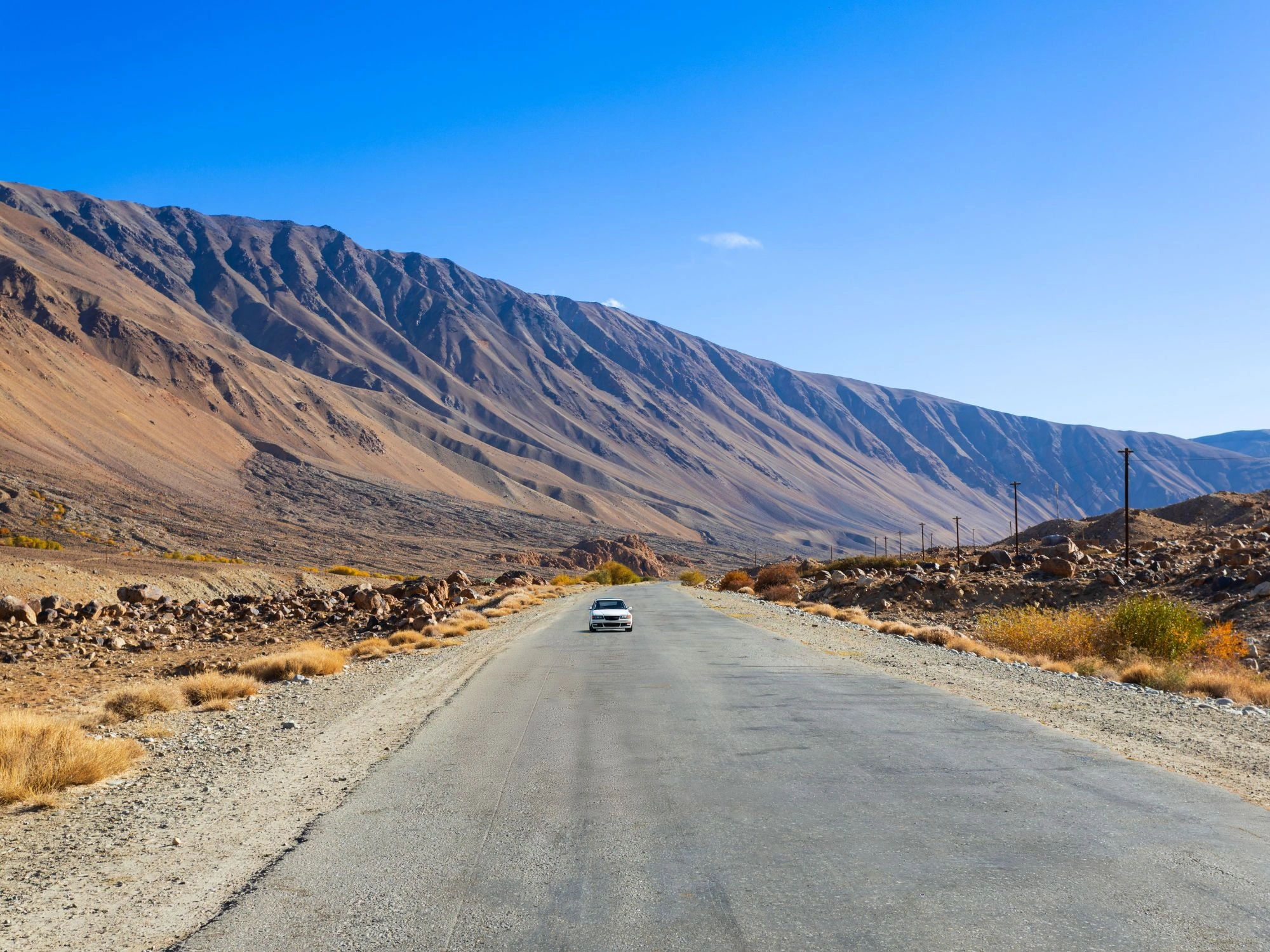 Car driving on a remote stretch of the Pamir Highway with rugged brown mountains in Tajikistan