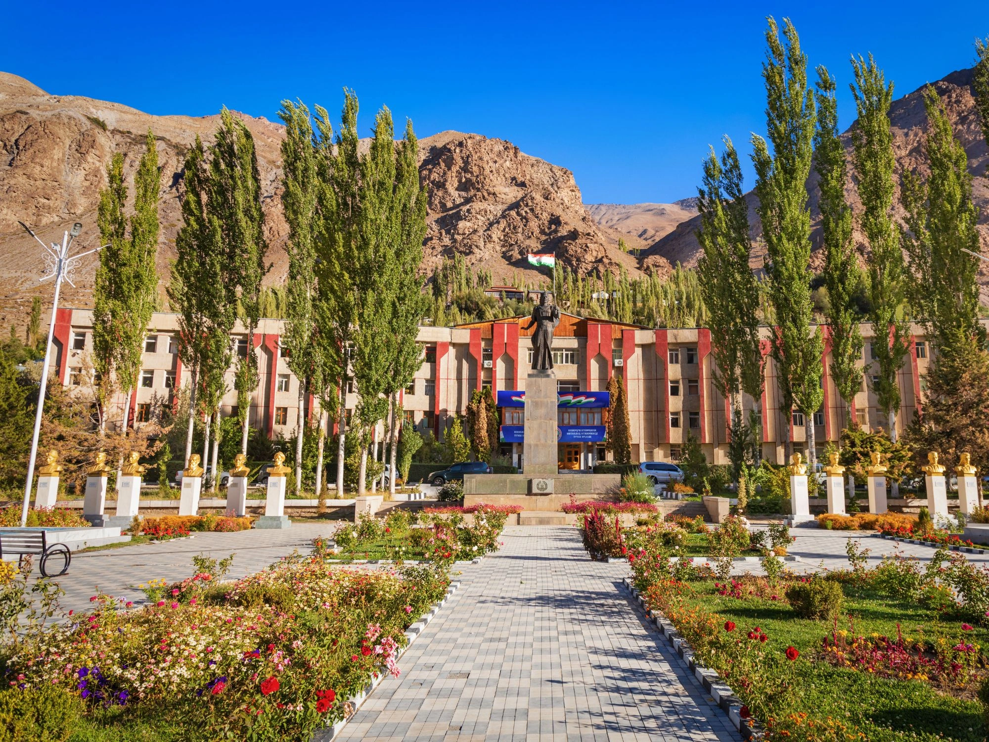 Khorog Town Hall and central monument with lush gardens, framed by mountains in Tajikistan.