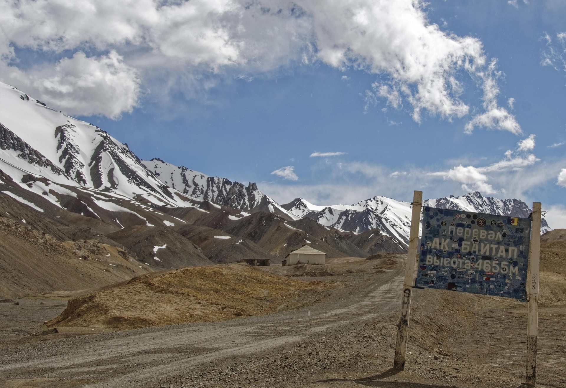 Sticker-covered Ak-Baital Pass sign at 4,655m, Tajikistan's highest point on the scenic Pamir Highway.
