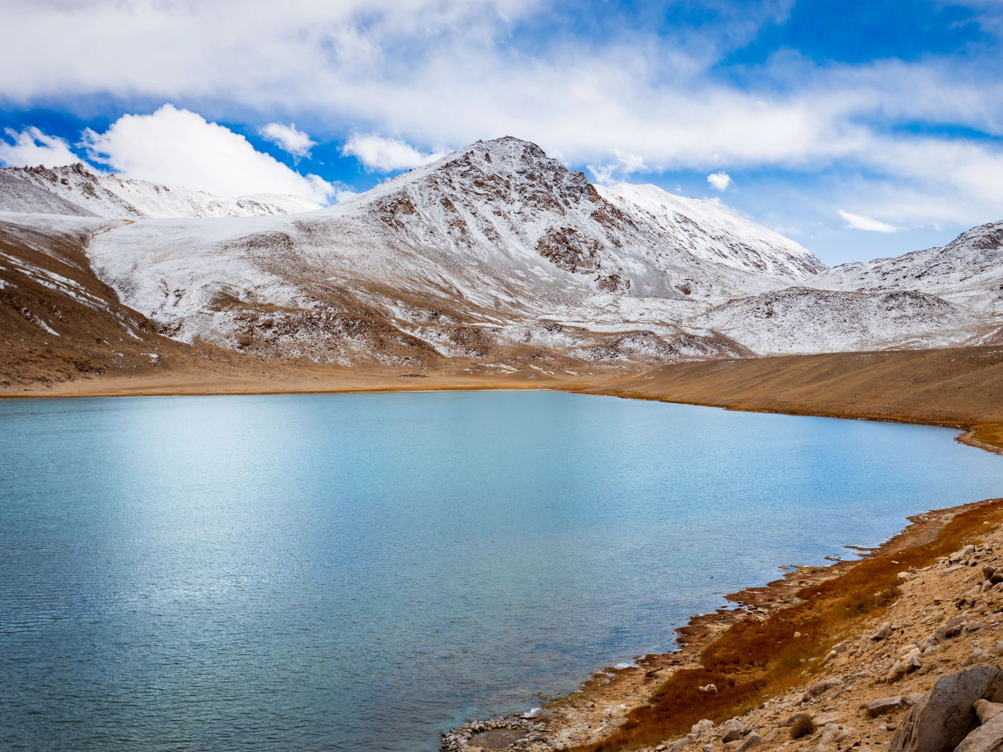 Turquoise mountain lake bordered by snow-dusted hills under a bright sky in eastern Tajikistan.