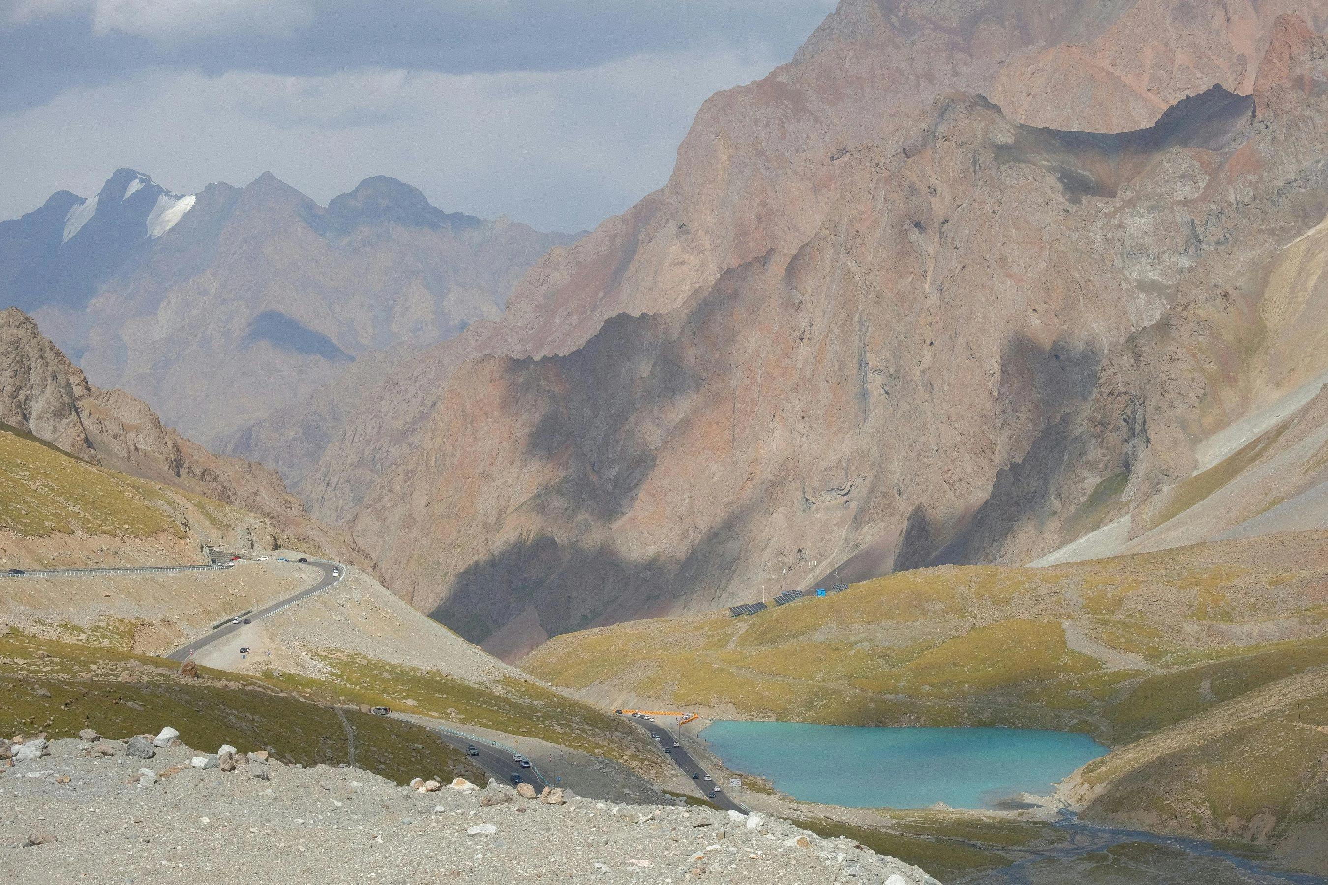 Curving road through rocky mountains with a turquoise alpine lake nestled below steep cliffs.