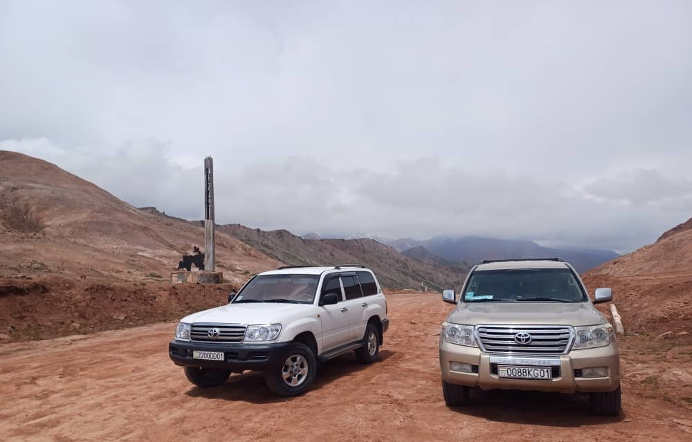 Two Toyota Land Cruisers at a high-altitude pass on the Pamir Highway, surrounded by barren peaks.