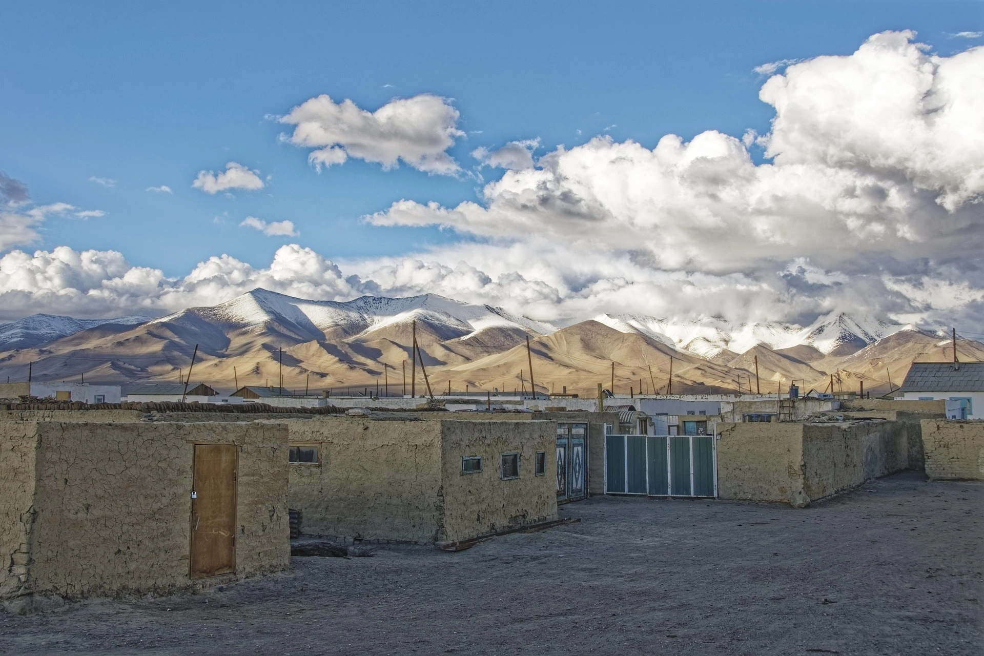 Traditional mud-brick homes in Murghab with dramatic snow-dusted Pamir Mountains in the background.