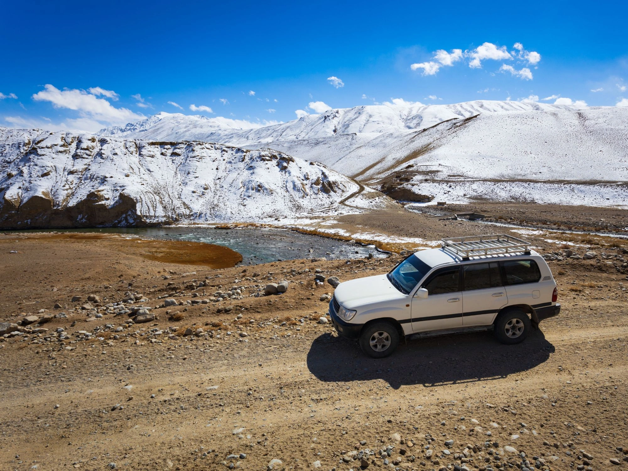 Toyota 4x4 parked beside a partially frozen river on the Pamir Highway's high-altitude route.