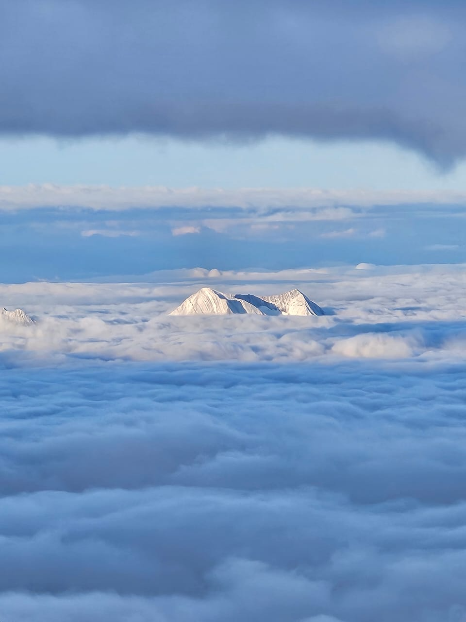 Isolated peak of Mount Kazbek rising above thick clouds at golden hour.