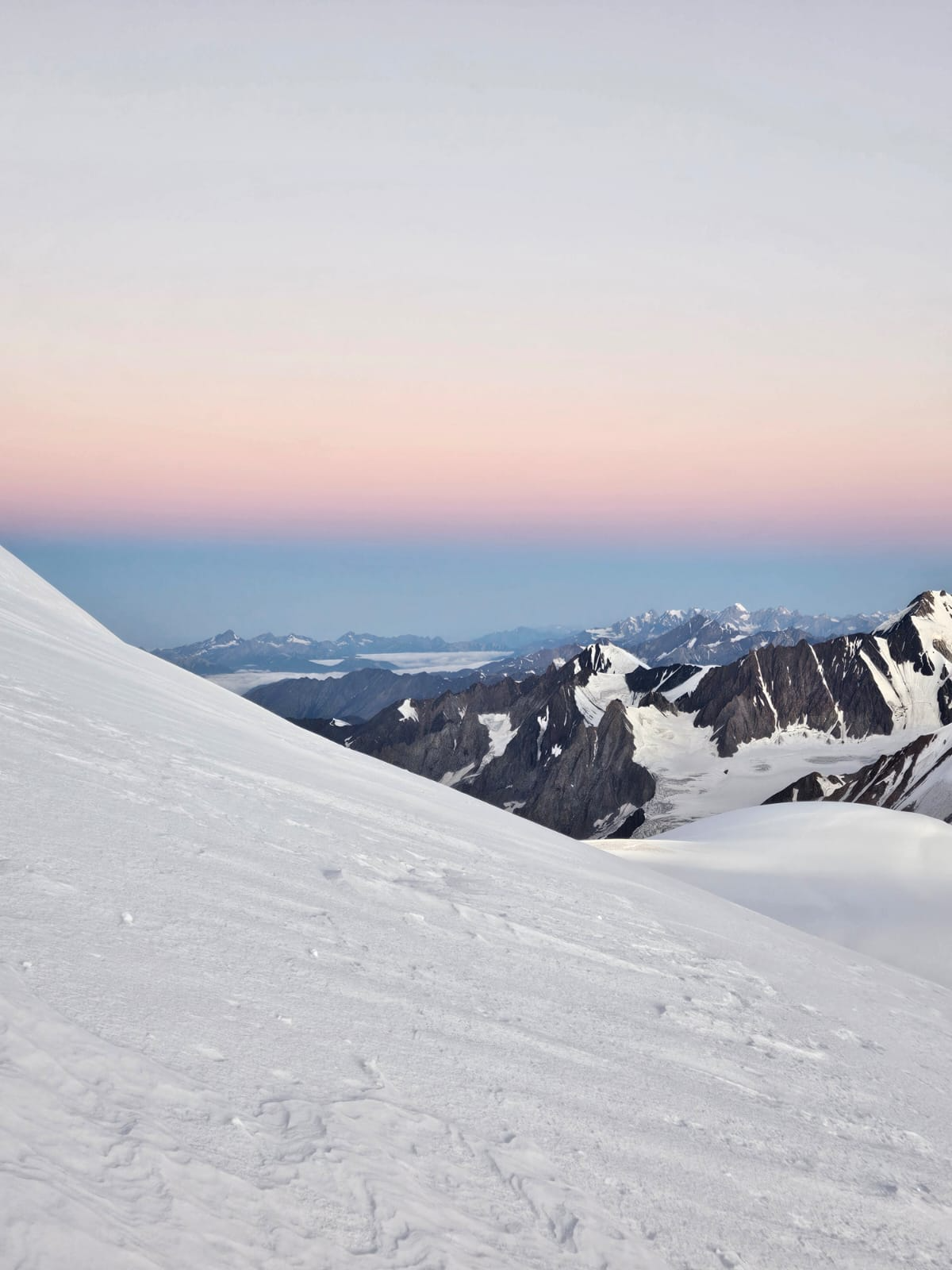 Wide snowy slope of Mount Kazbek with pastel horizon and rugged mountain backdrop.
