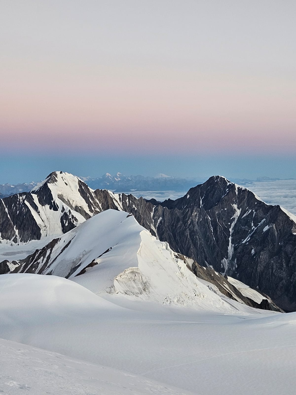 Pink and blue alpenglow over jagged Mount Kazbek peaks and glaciers at sunrise.
