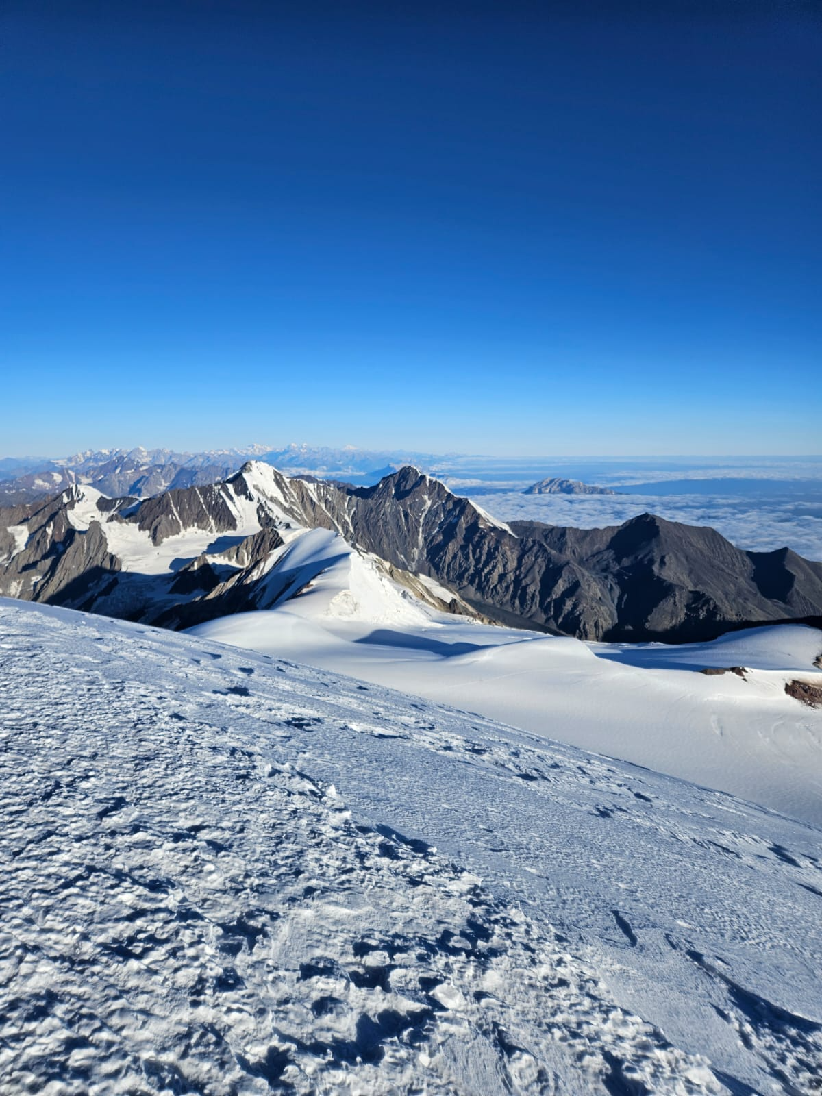 Snowy peak of Mount Kazbek with rugged Caucasus mountains in clear blue daylight.