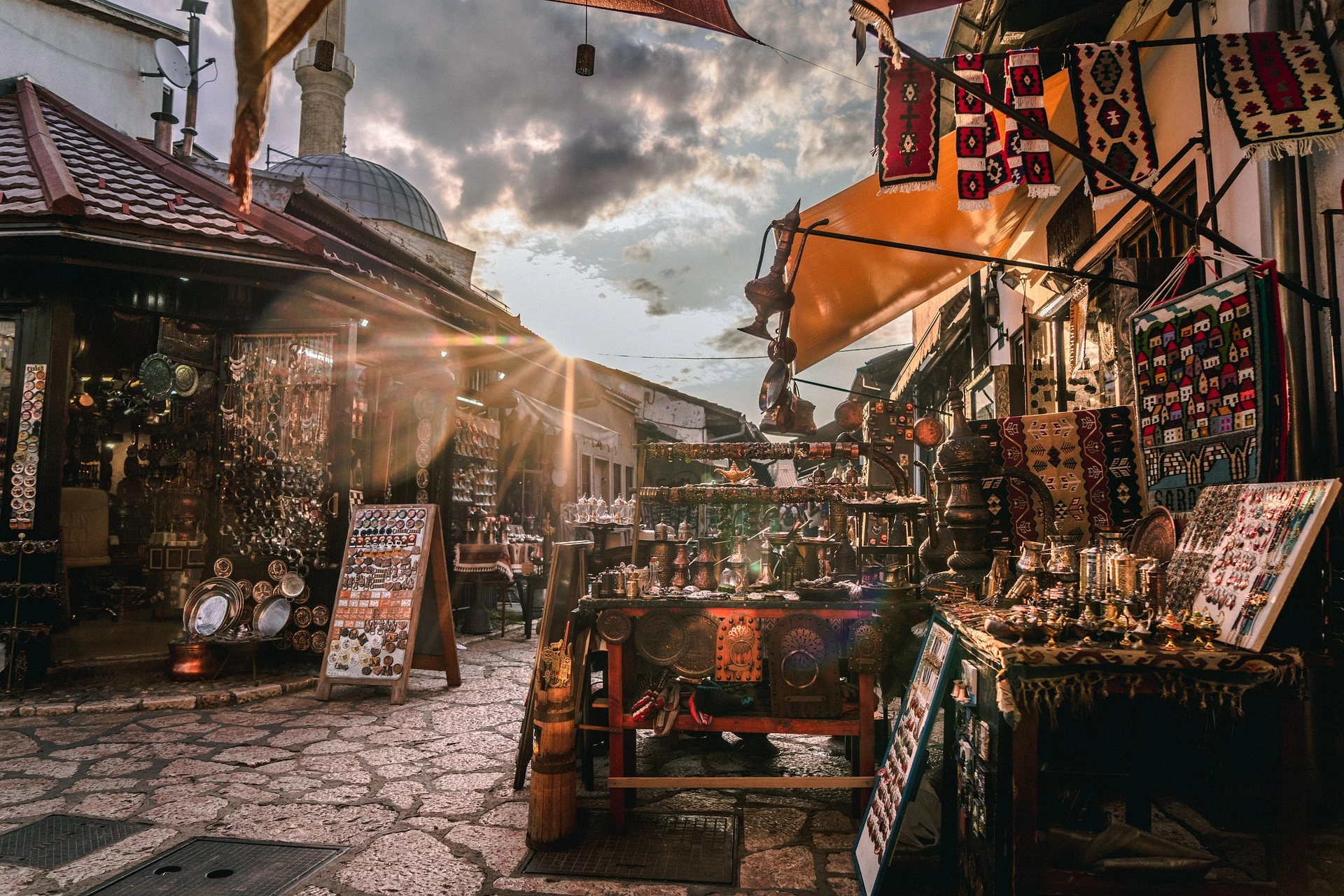 Bustling Sarajevo bazaar at sunset, filled with colorful carpets, jewelry, and copper crafts.