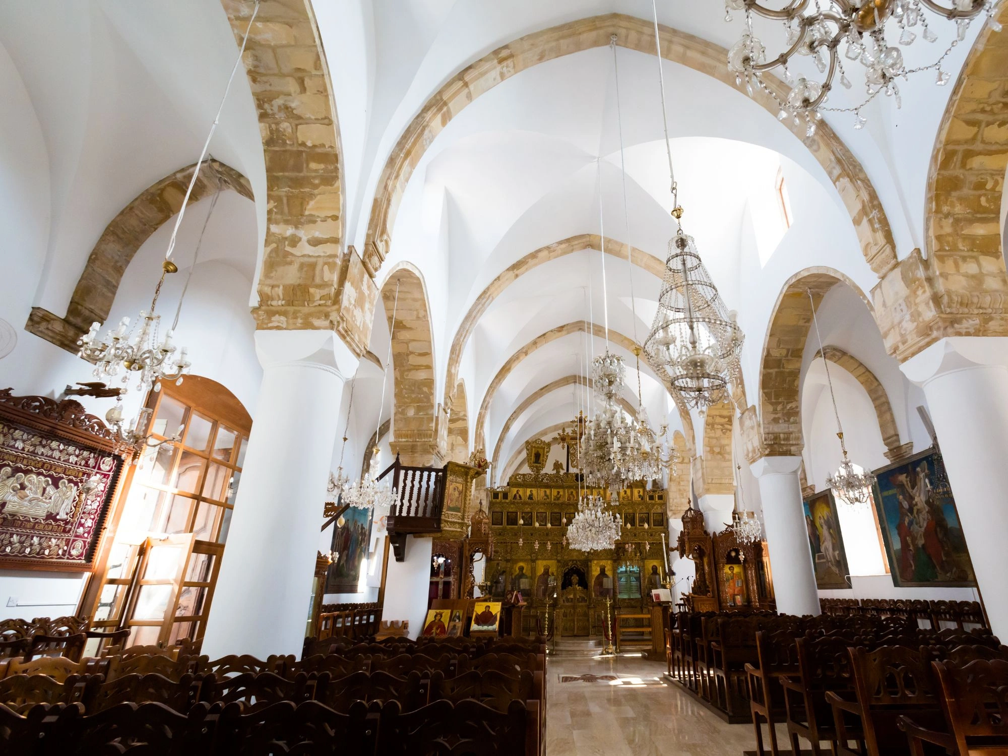 Ornate interior of a Greek Orthodox church in Cyprus with chandeliers and arches.