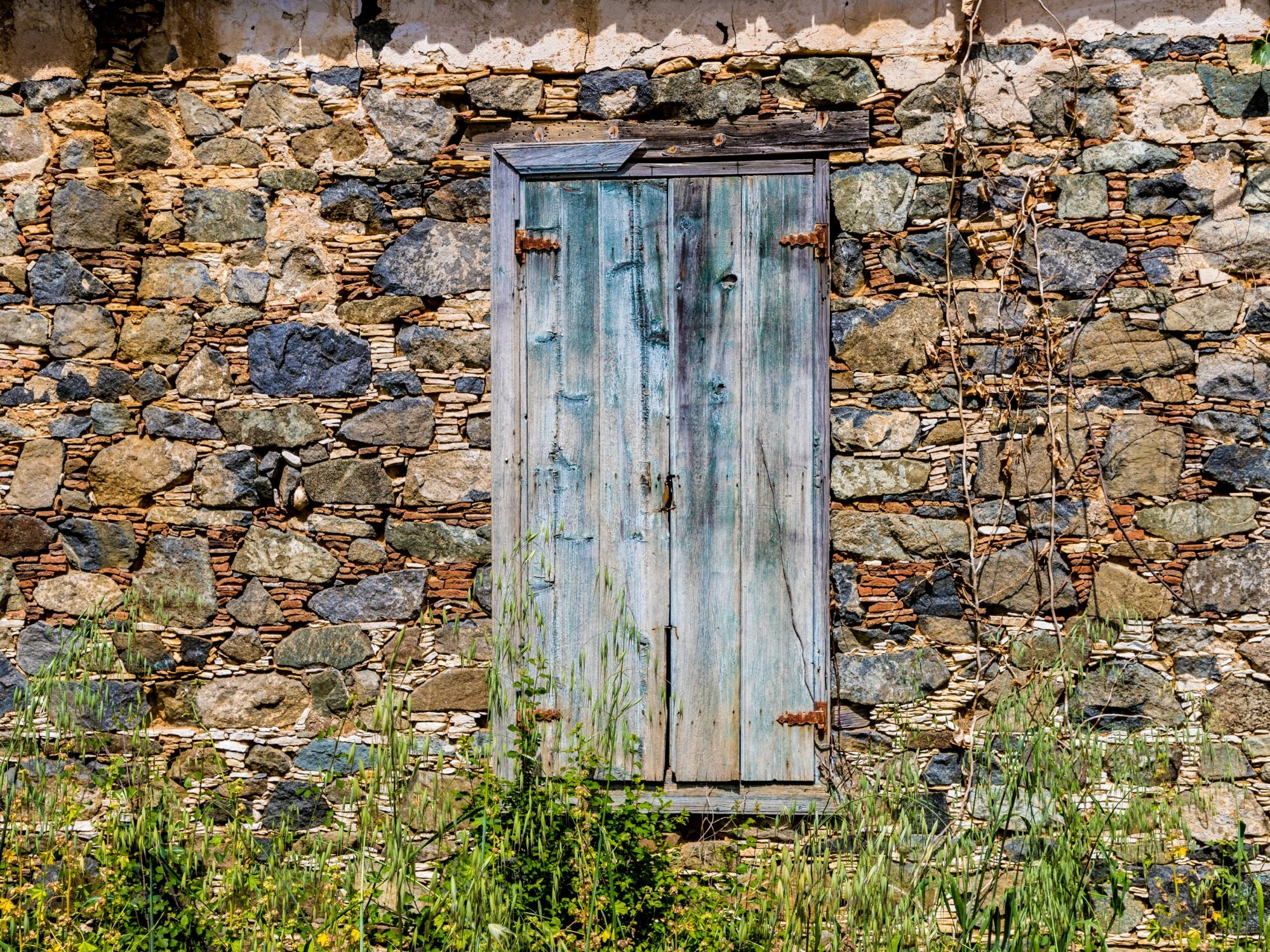 Stone wall with blue wooden window in Omodos village, Cyprus countryside charm.