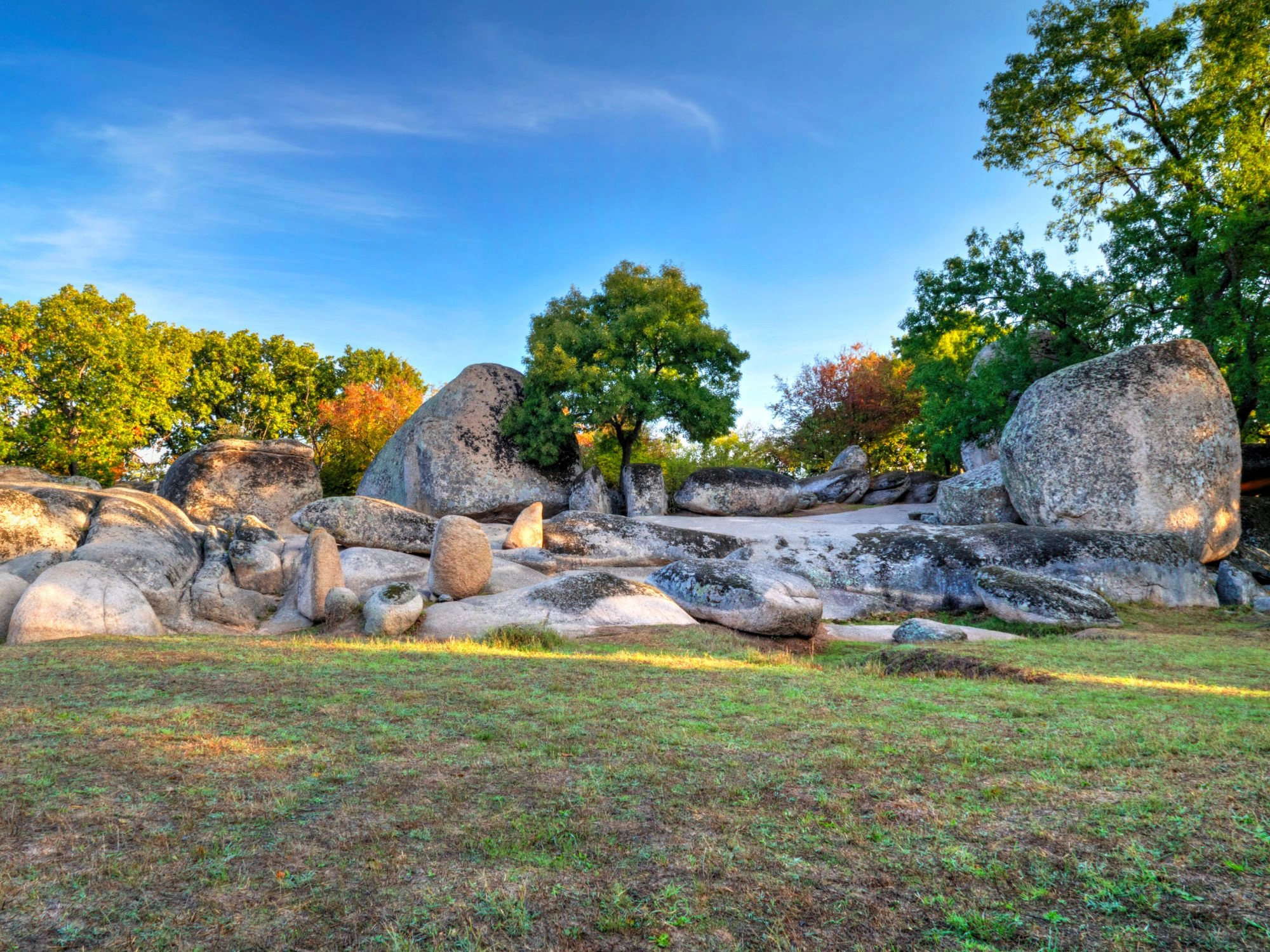 Granite megaliths and boulders scattered across a lush green field at sunset.