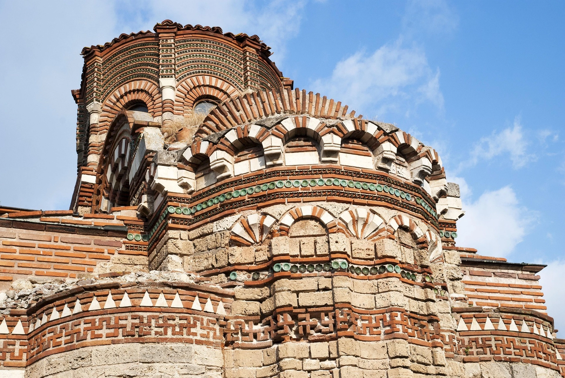 Detailed exterior of the church of Christ Pantocrator in Nessebar with red brick arches and decorative green accents.