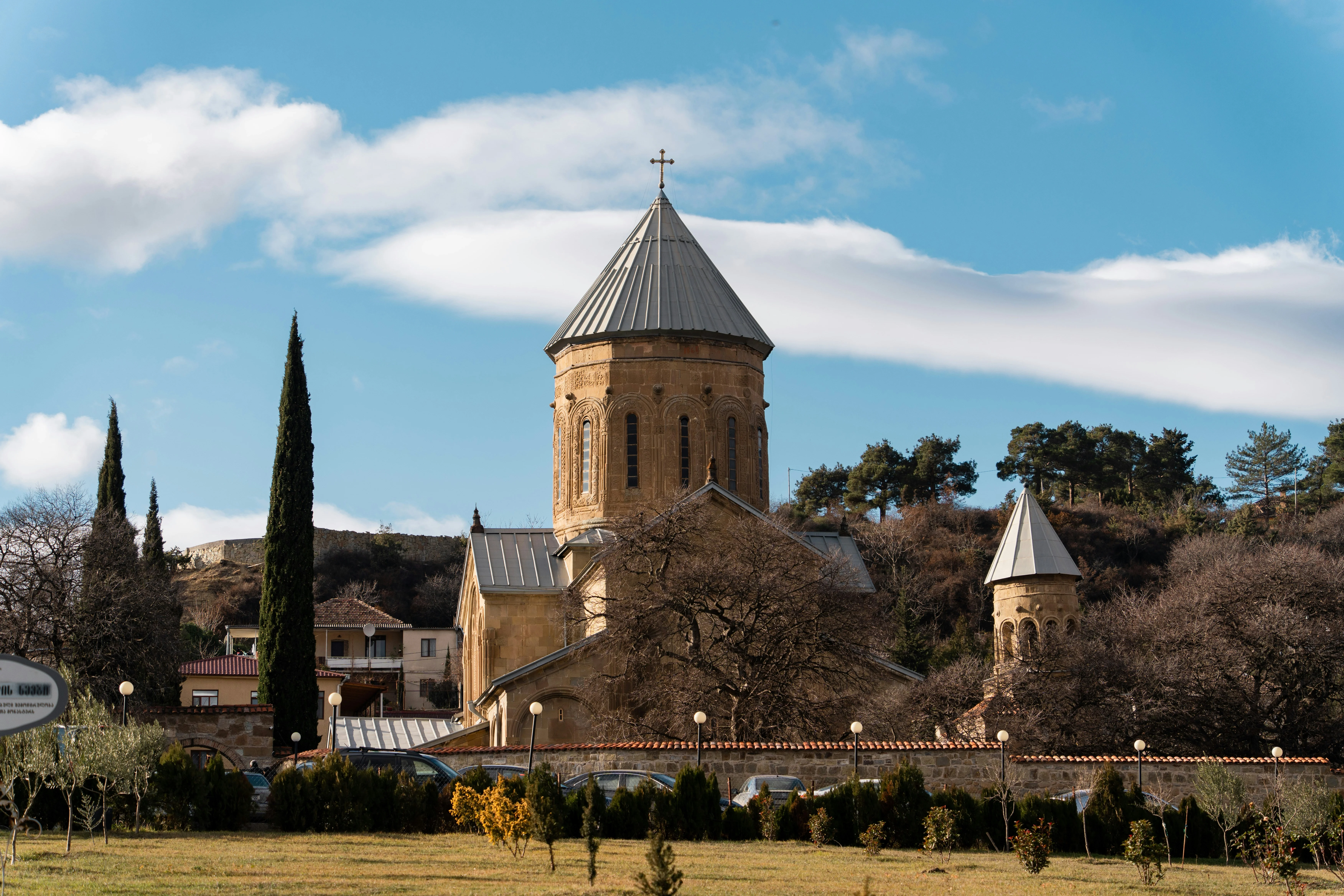 onastery with conical dome and cross in Mtskheta, Georgia, surrounded by trees and clear skies.