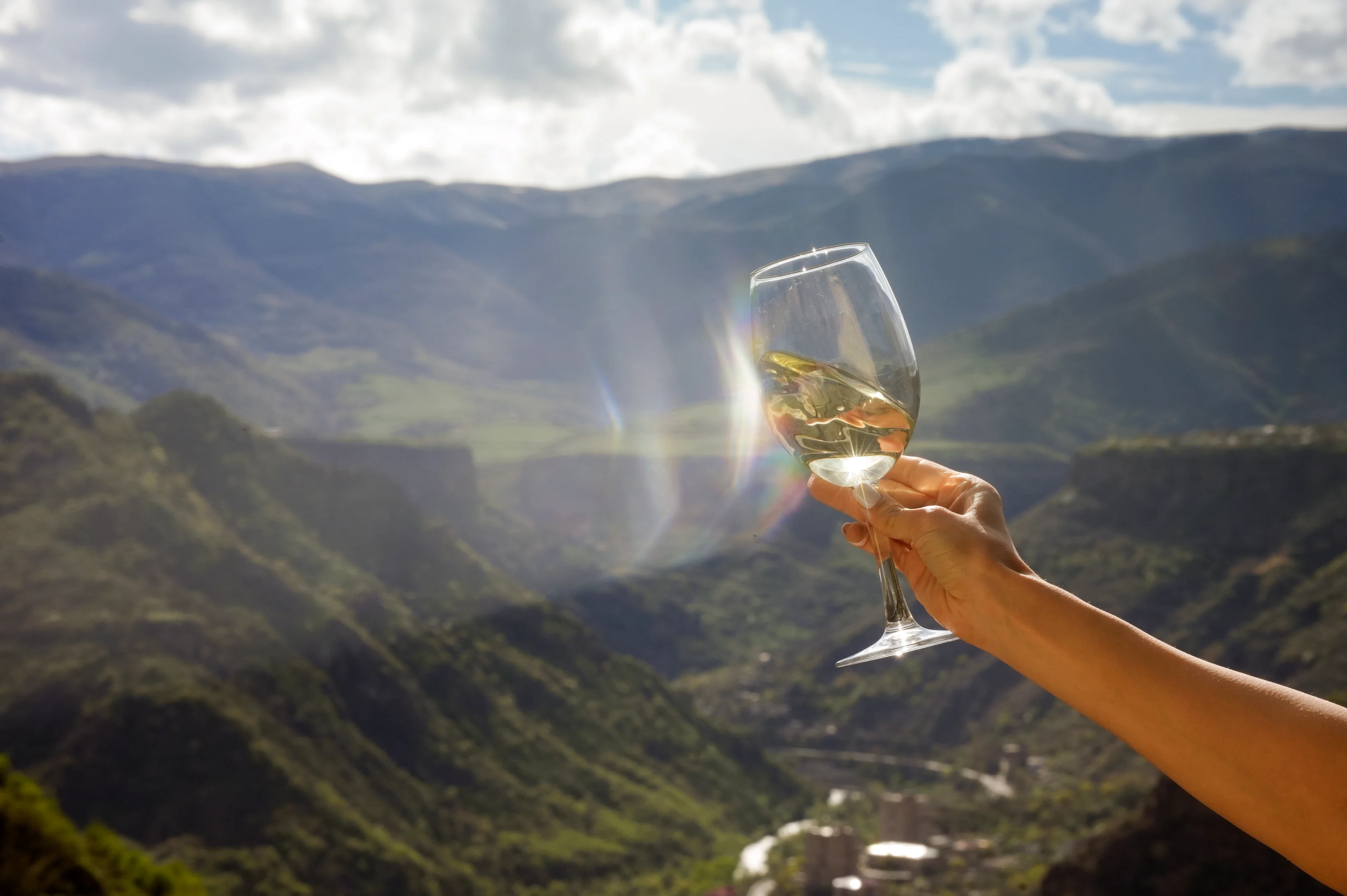 Hand holding a glass of white wine against the scenic mountain landscape of Armenia’s Lori region.