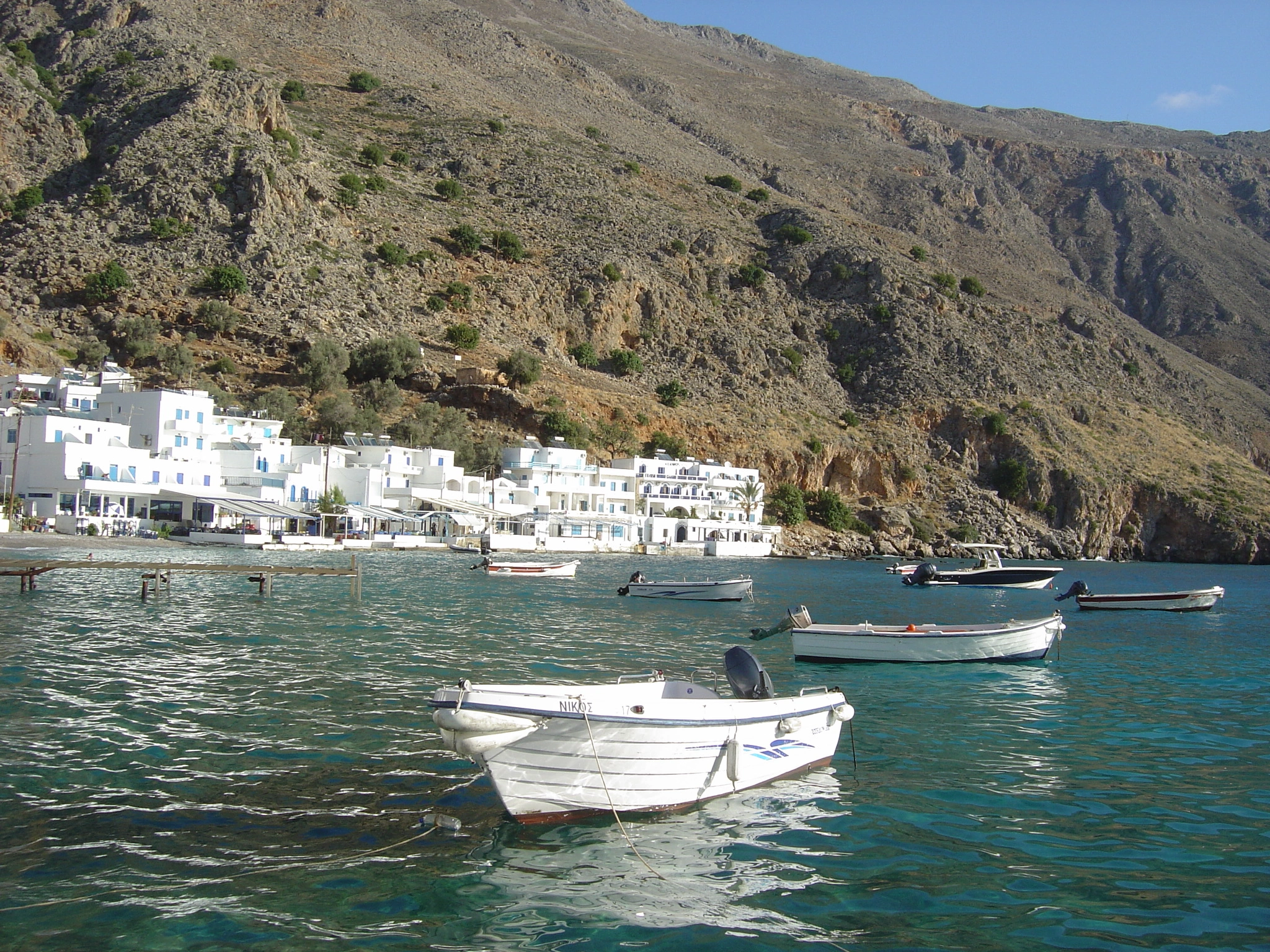 Boats anchored near whitewashed buildings of Loutro village along Crete’s rocky coastline.