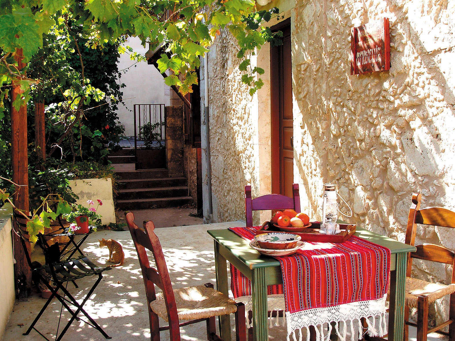 Shaded patio in Vamos village with pomegranate-filled table and rustic charm.