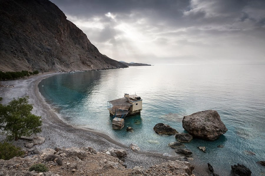 Isolated seaside hut sits in turquoise bay below dramatic cliffs on Crete’s south coast.