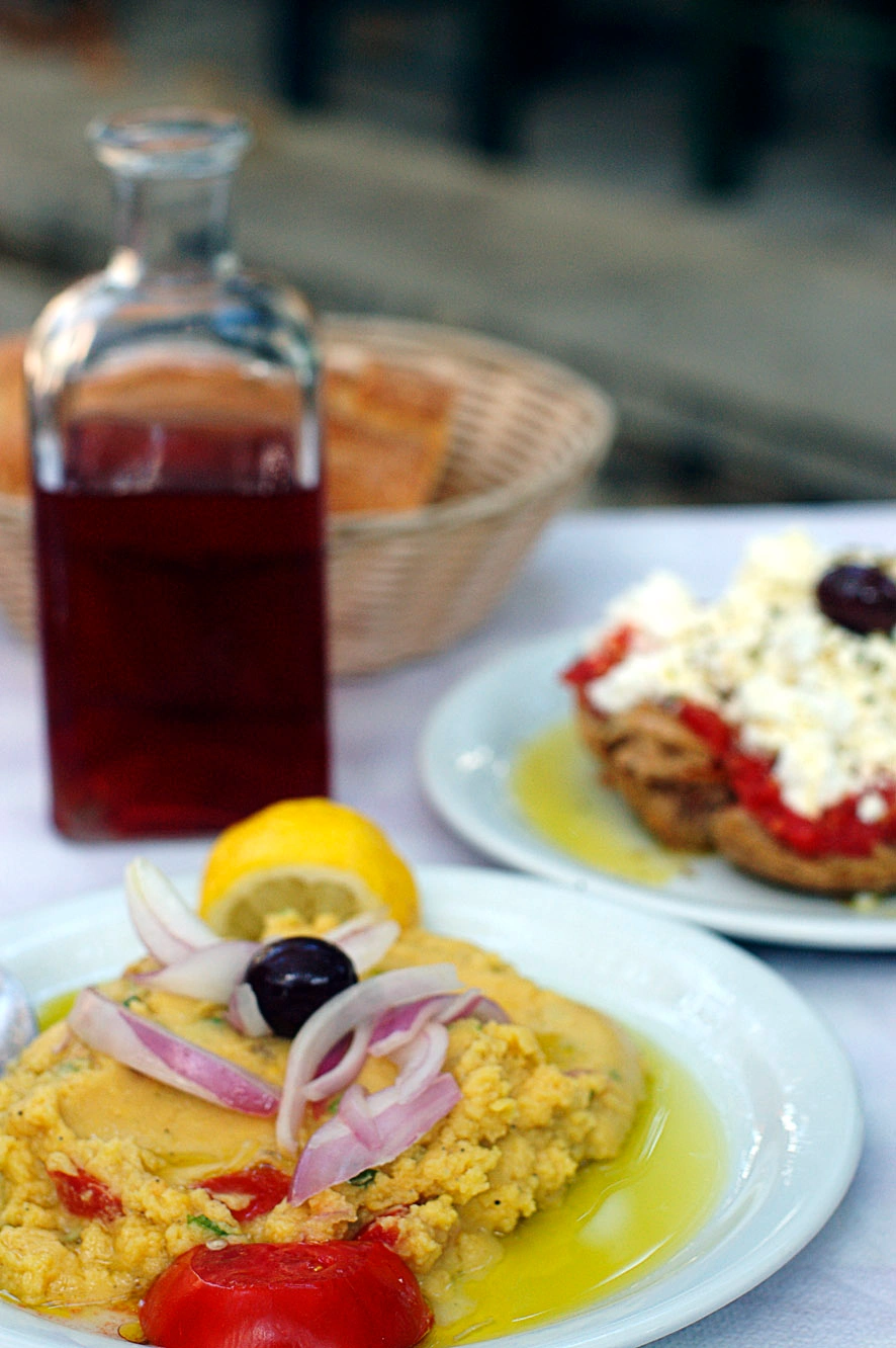 Close-up of Cretan fava with onions, olives, tomato, and olive oil served with bread and wine.