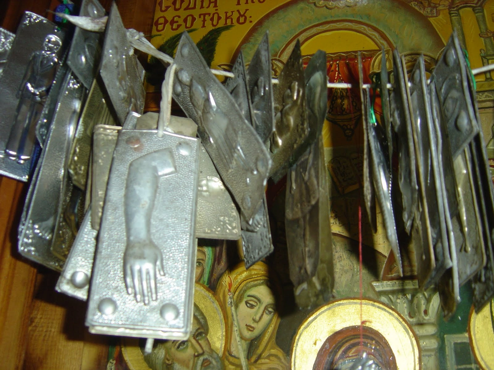 Silver religious votive offerings with body parts hang in front of Orthodox icons.