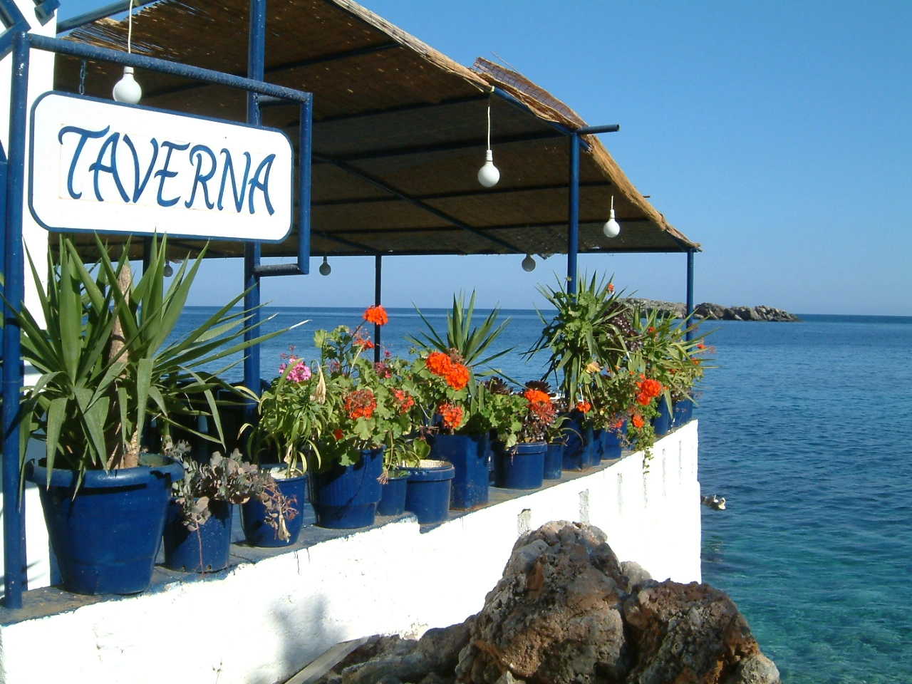 Seaside taverna in Loutro, Crete, decorated with flowers and blue pots by the water.