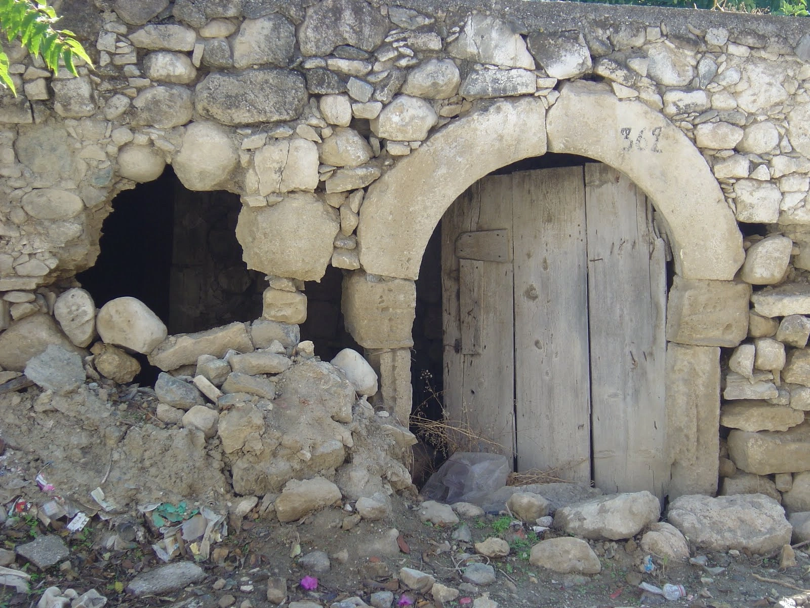 Abandoned stone house with an arched wooden door and crumbling wall in Petrokefali village.