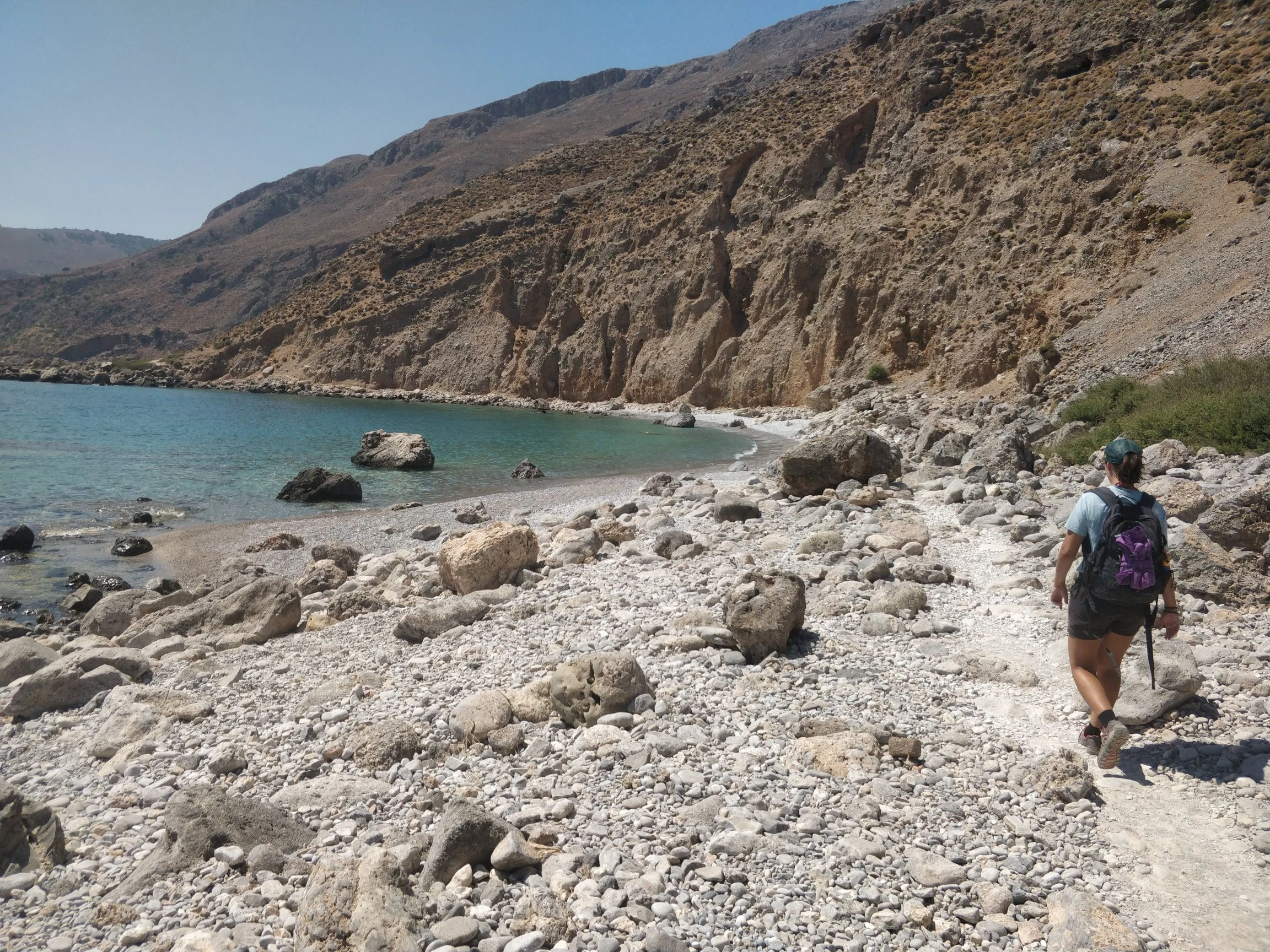 Hiker walks a rocky path by turquoise waters on Crete’s rugged south coast trail.