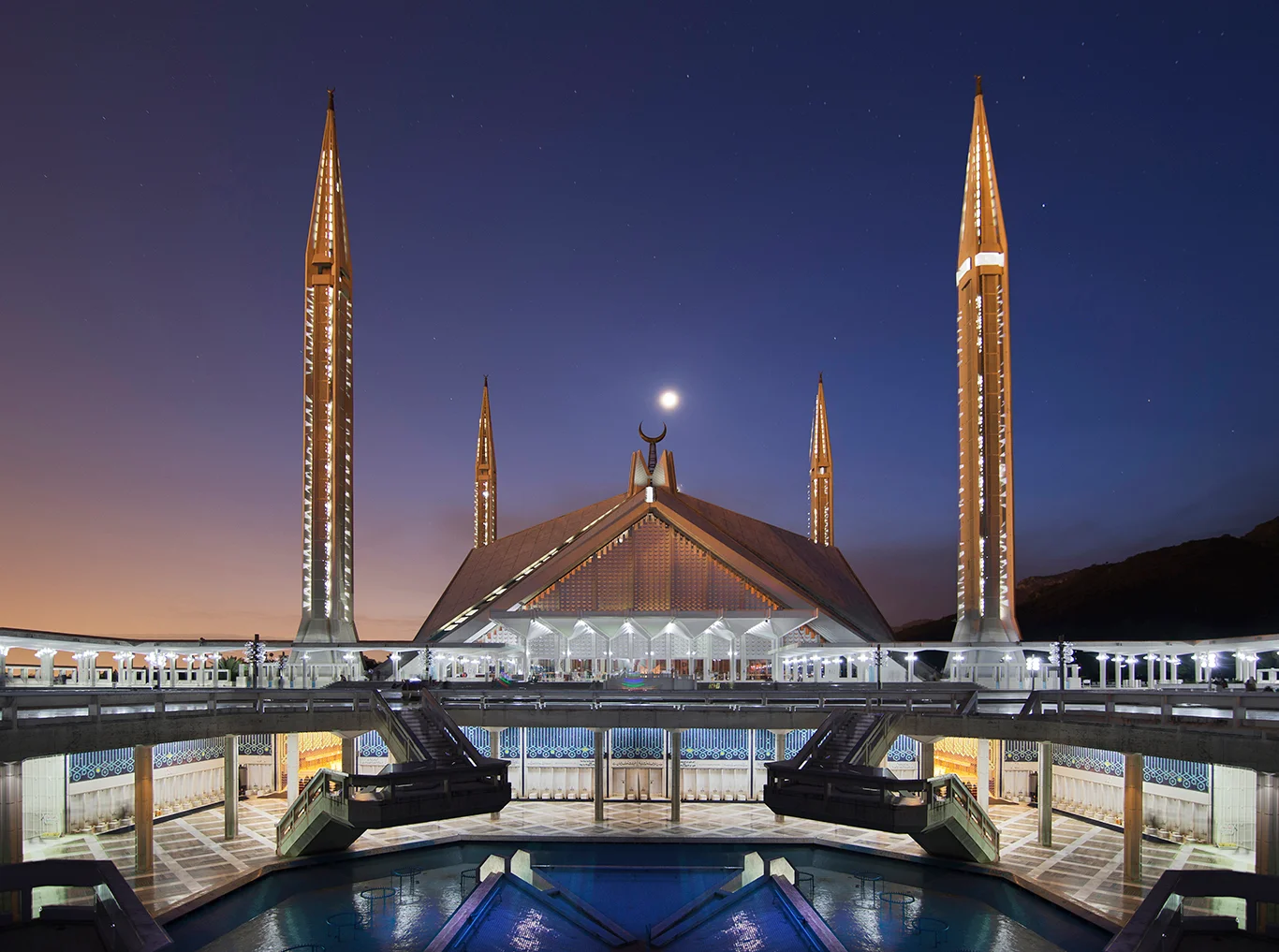 Night view of Faisal Mosque Islamabad, lit up minarets and crescent moon above the roof.