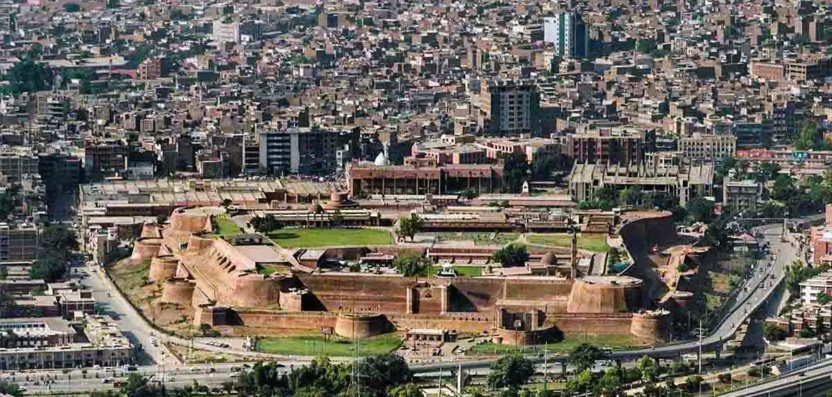 Aerial view of Balahisar Fort Peshawar, historic red brick fortress in busy city landscape.