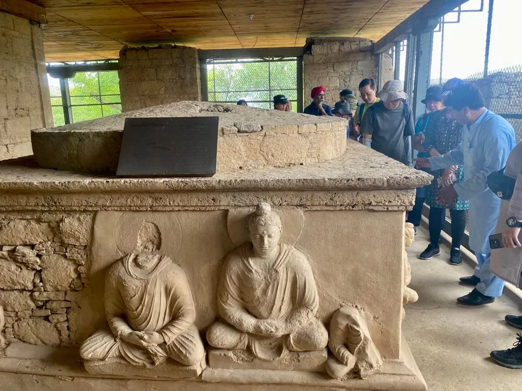 Taxila Museum stupa with Buddha carvings, tourists exploring historic Gandhara art.