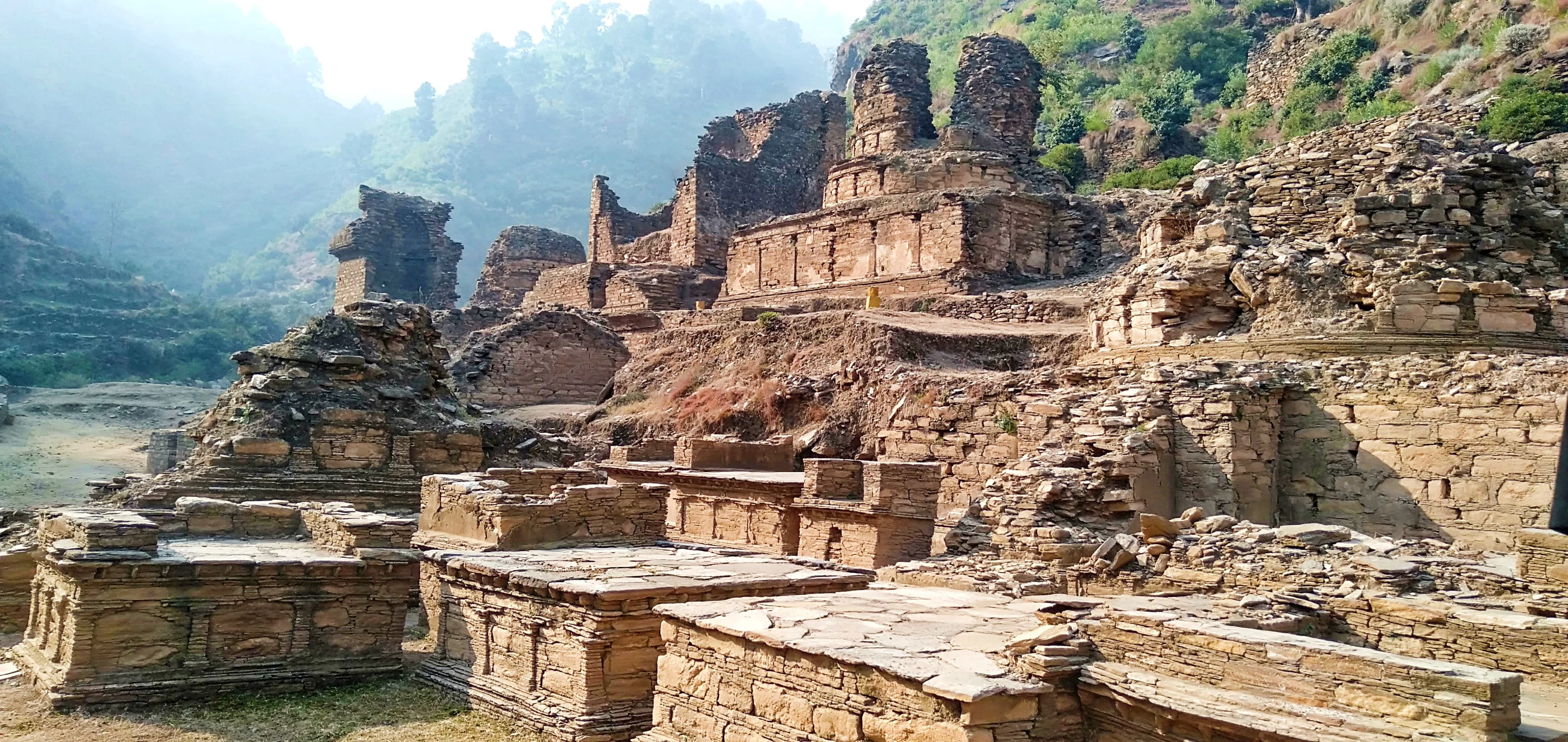 Abasahib Cheena ruins in Pakistan surrounded by green hills, ancient Buddhist archaeological site.
