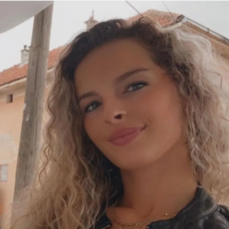 Eine junge Frau mit blonden, lockigen Haaren lächelt in die Kamera.