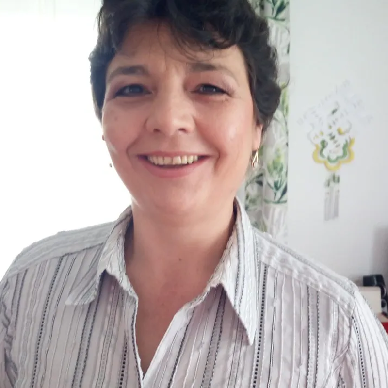Eine Frau mit dunklen, kurzen Haaren im weißen Oberteil lächelt in die kamera.