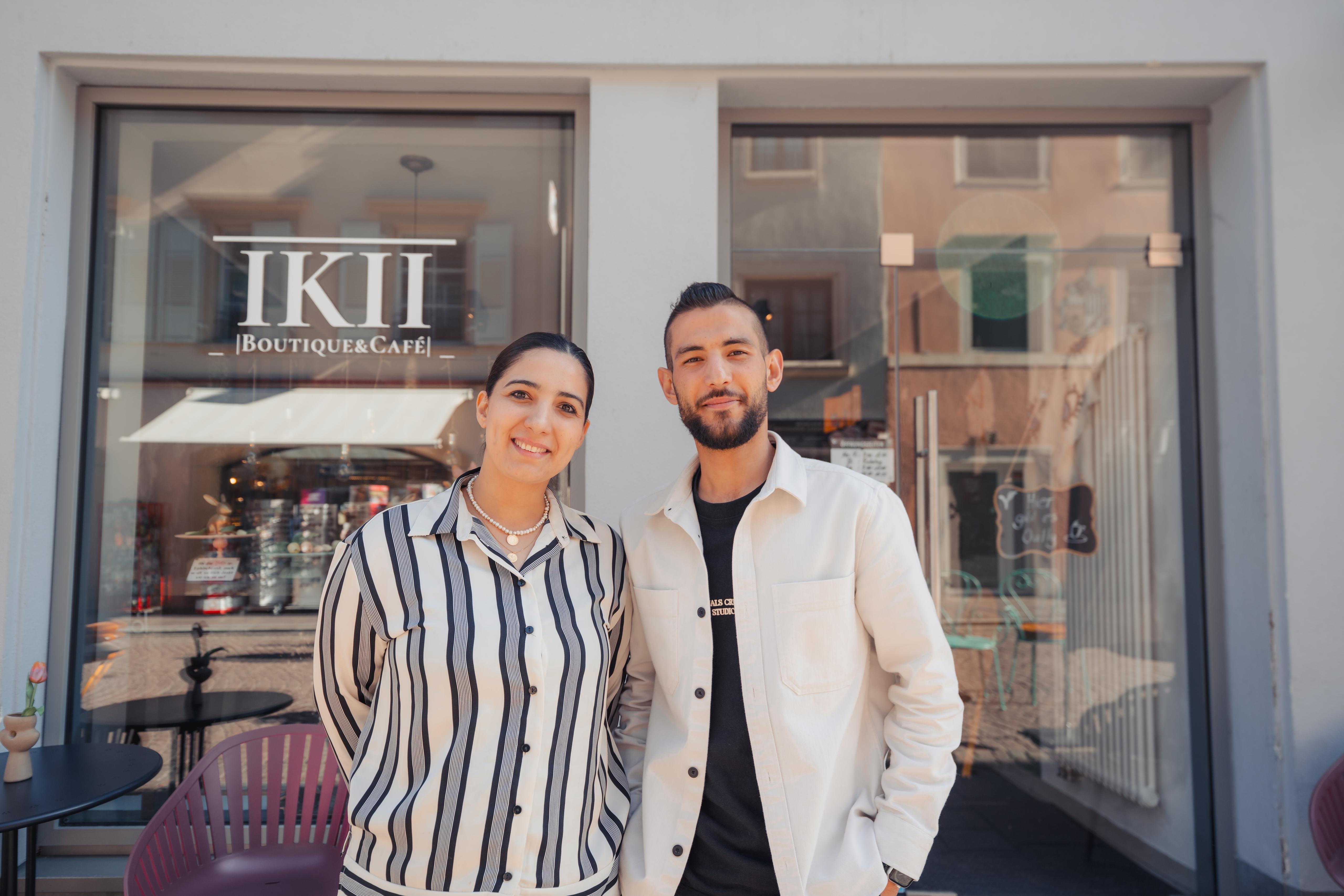 Zwei Personen stehen lächelnd vor dem Eingang von IKII Boutique & Café.