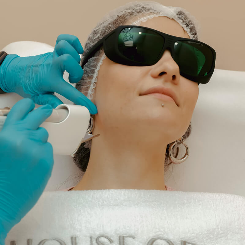 Frau mit Sonnenbrille bekommt Hautanwendung im Gesicht.