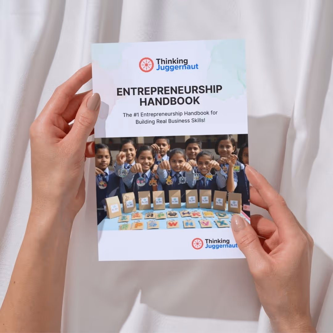 Person holding the Entrepreneurship Handbook by Thinking Juggernaut with a group of children displaying handmade products on the cover.
