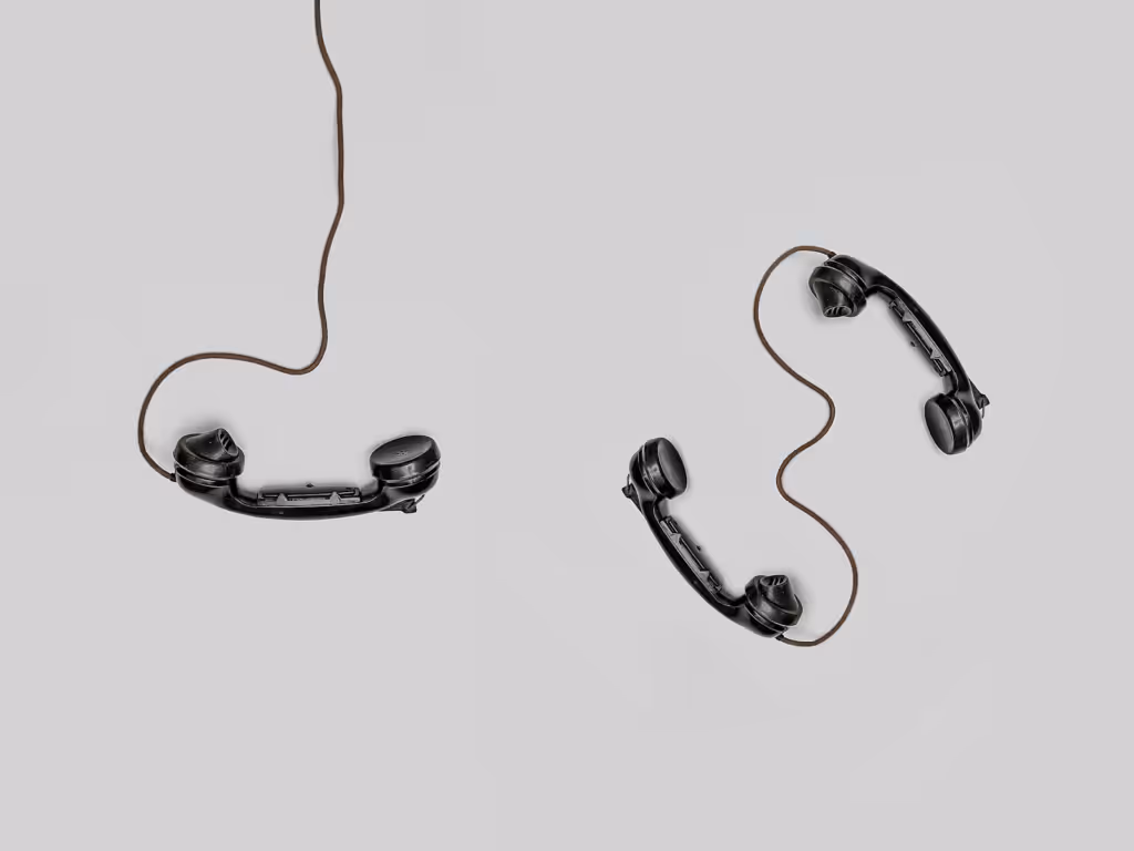 Two black vintage telephone receivers connected by a single cord on a plain grey background