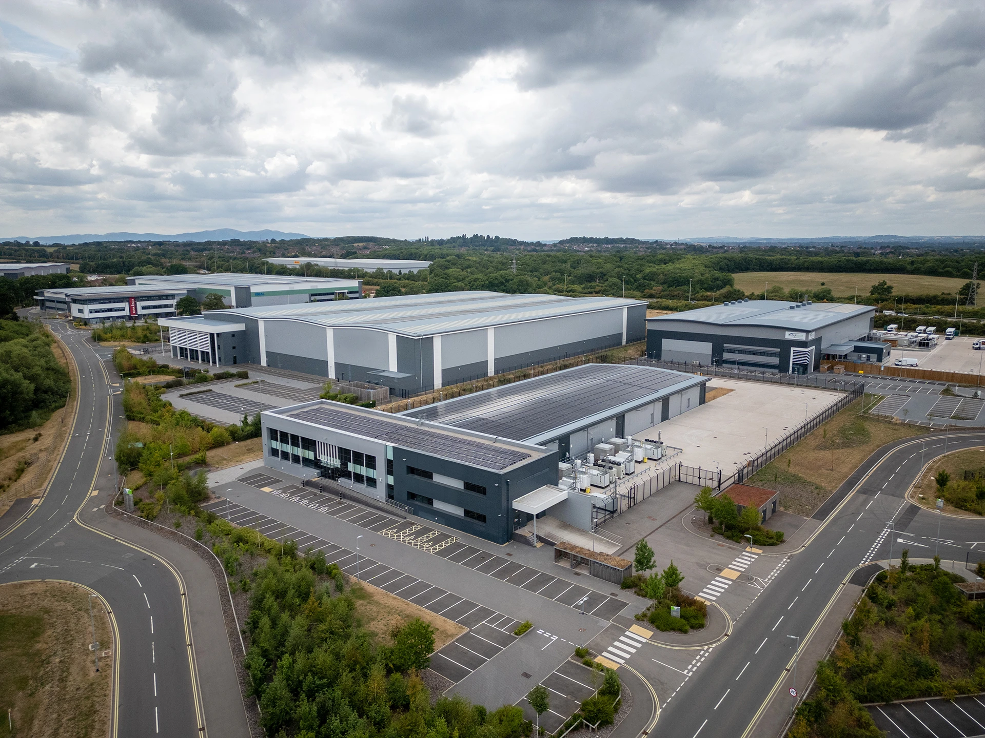 Aerial view of industrial warehouse complex with rooftop solar panel installations in rural setting