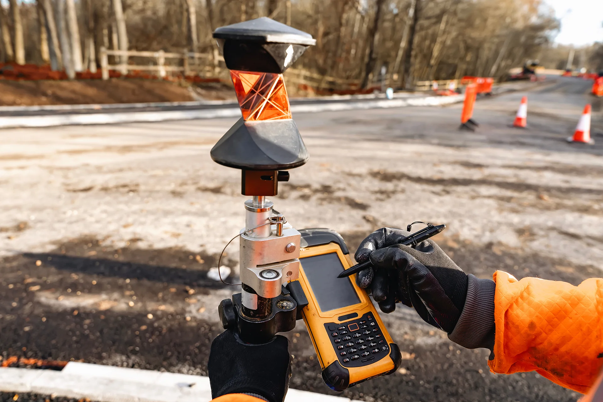 Land surveyor operating GPS surveying equipment at a road construction site.