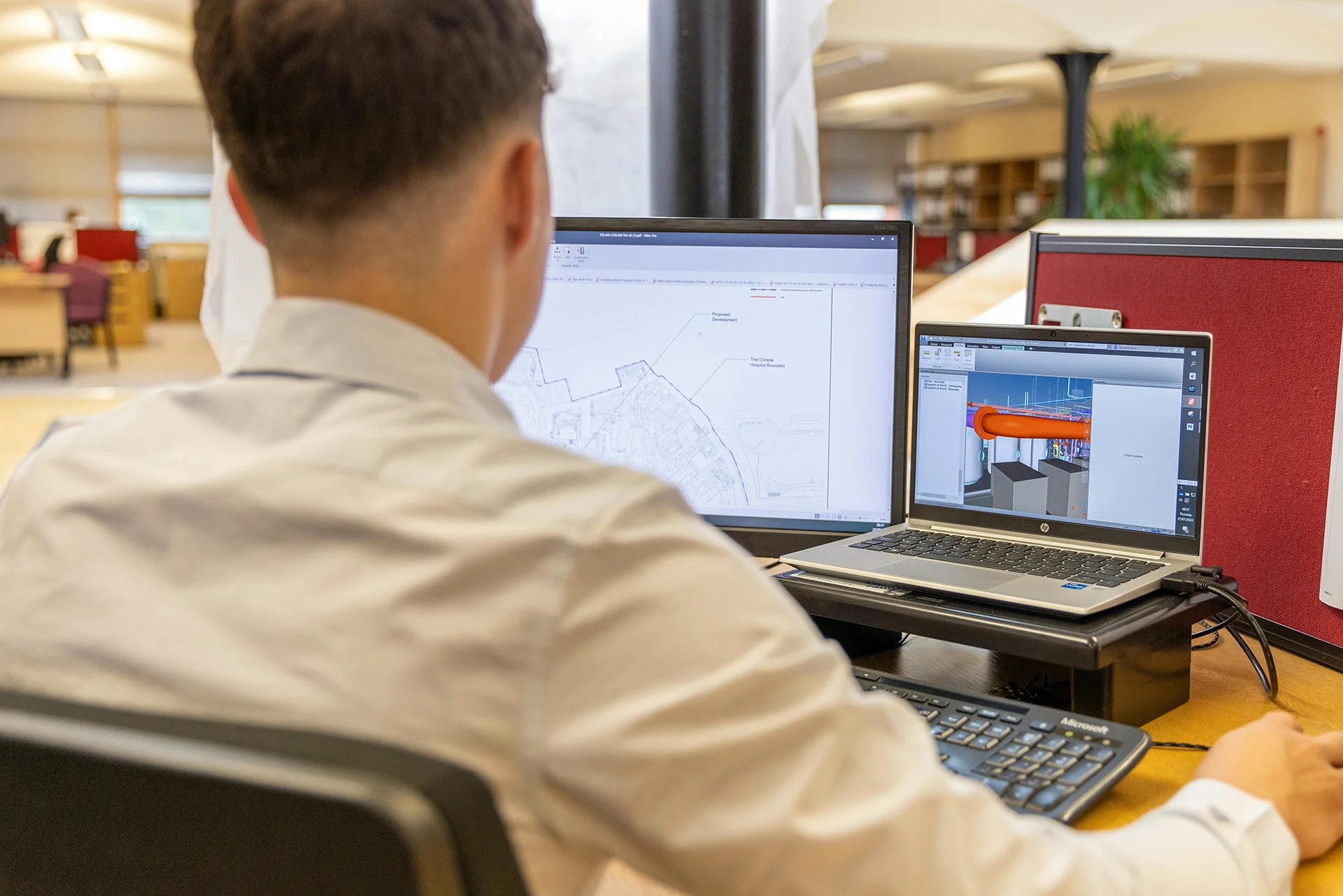 Engineer reviewing CAD designs and 3D models on dual computer monitors in an office.