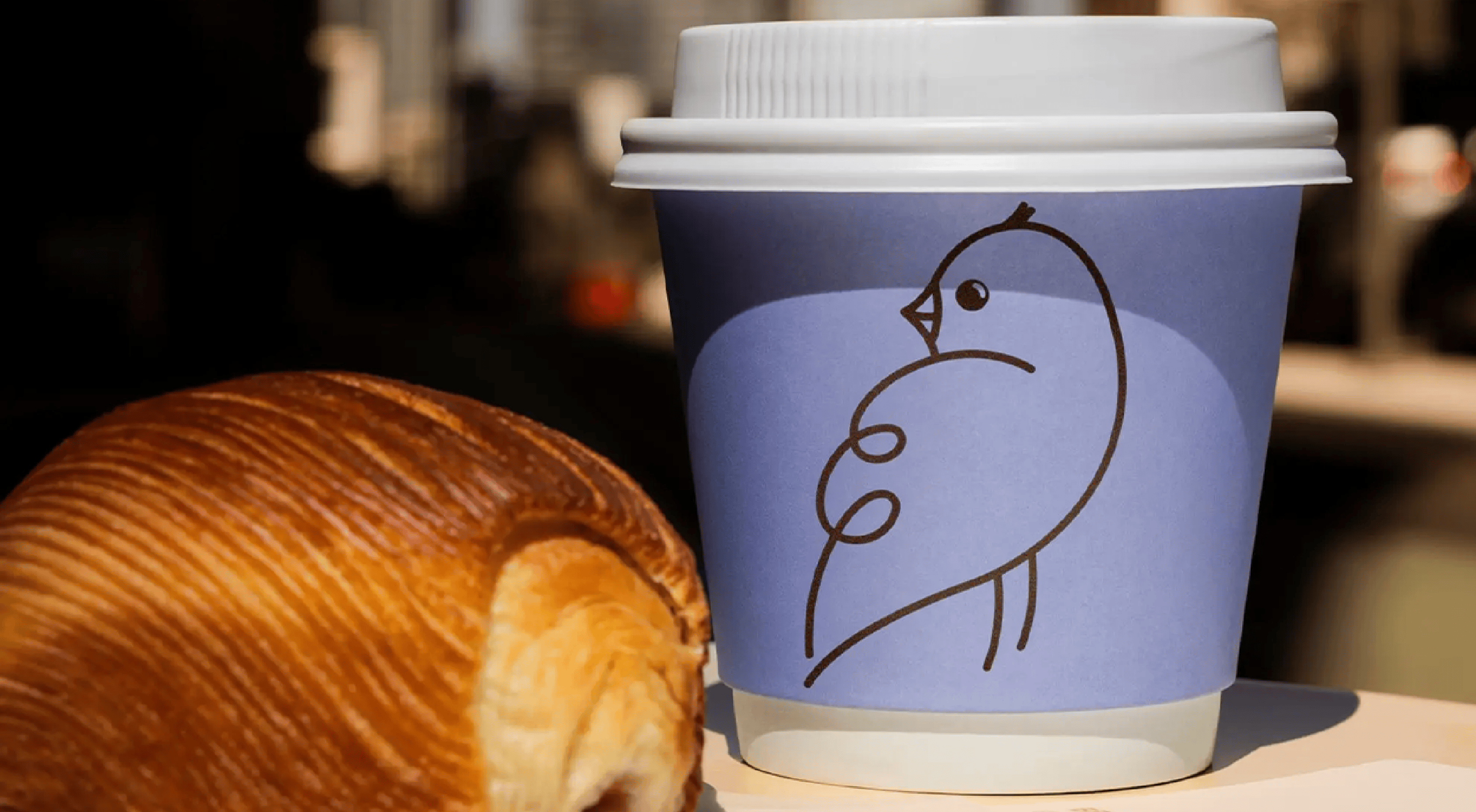 Birdee logo on purple disposable coffee cup and a croissant
