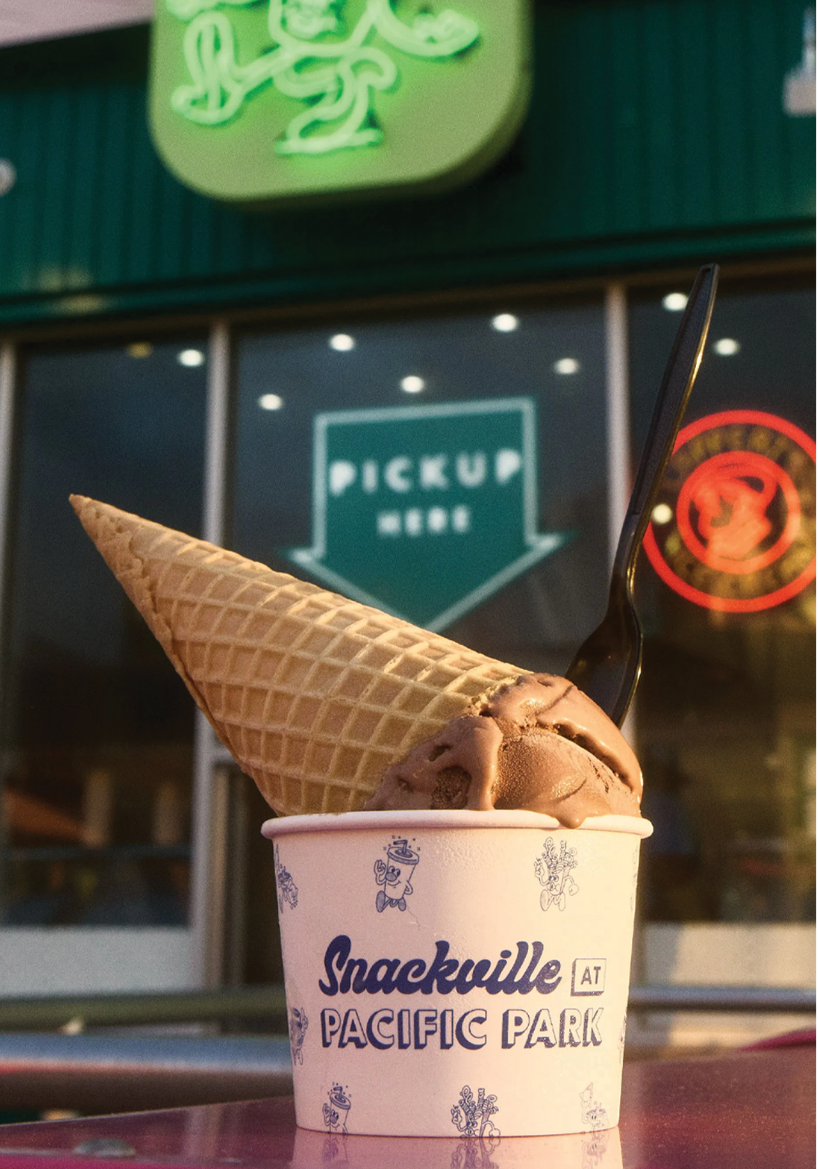 closeup of chocolate ice cream in a waffle cone upside down in a cup that has the Snackville logo on it