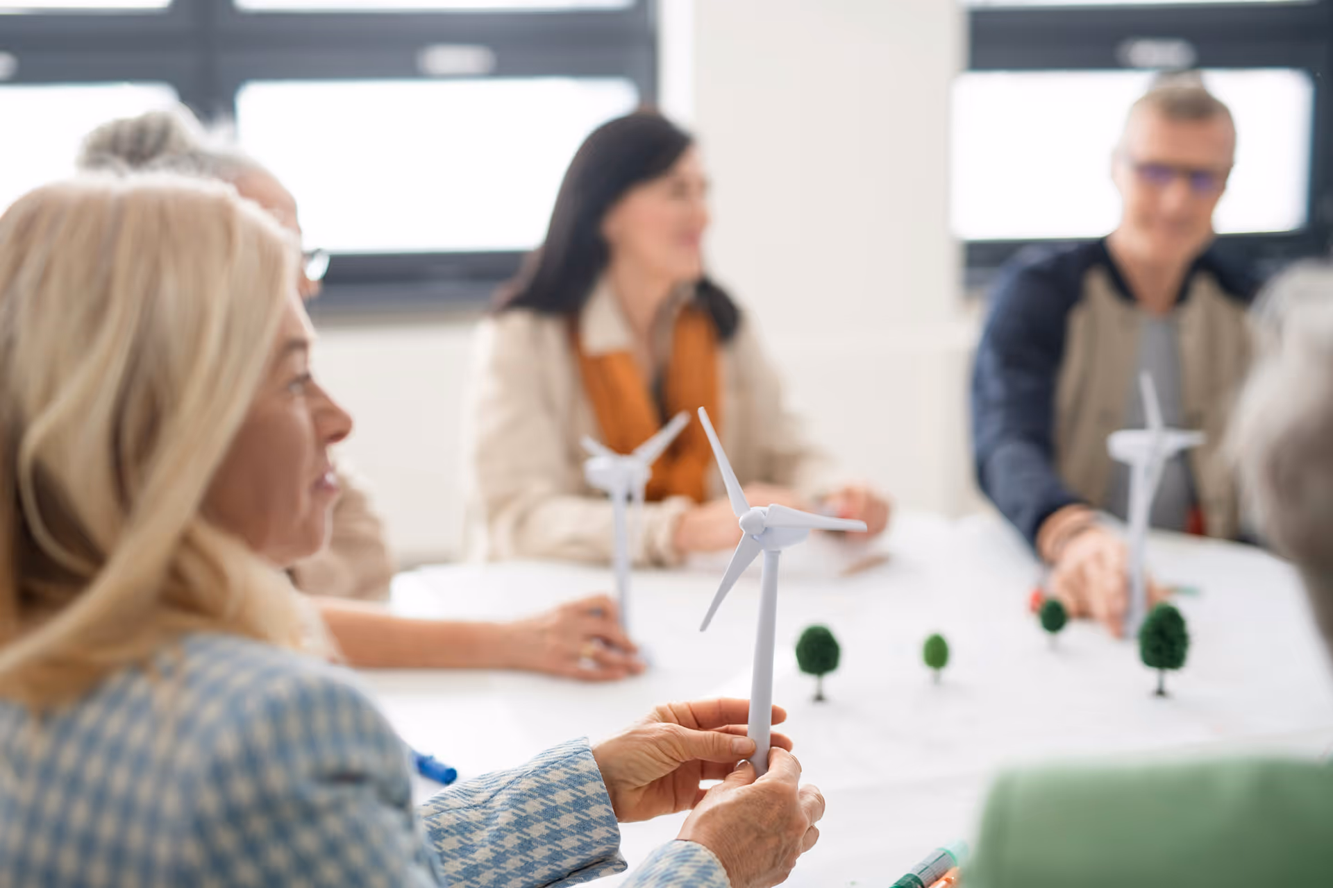 Personen an einem Tisch mit Windradmodellen und Miniaturbäumen bei einem Workshop
