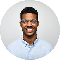 Smiling man with short curly hair and glasses wearing a light blue button-up shirt.