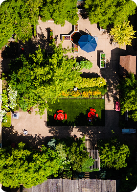 Aerial view of a garden with green trees, red flowers, a blue umbrella, and paved pathways.