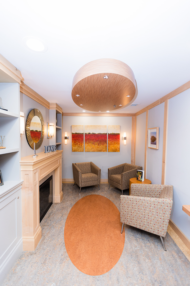 Small seating area with three patterned armchairs around a wooden side table, a light wood fireplace, abstract artwork on the wall, and a circular wooden ceiling fixture.